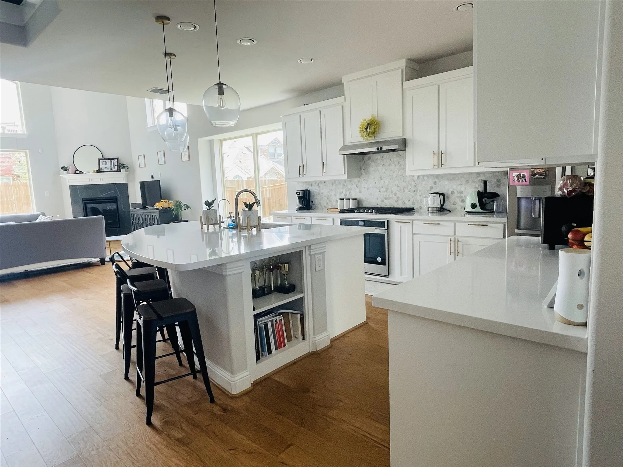 Kitchen featuring a kitchen island with sink, exhaust hood, oven, decorative light fixtures, and white cabinetry