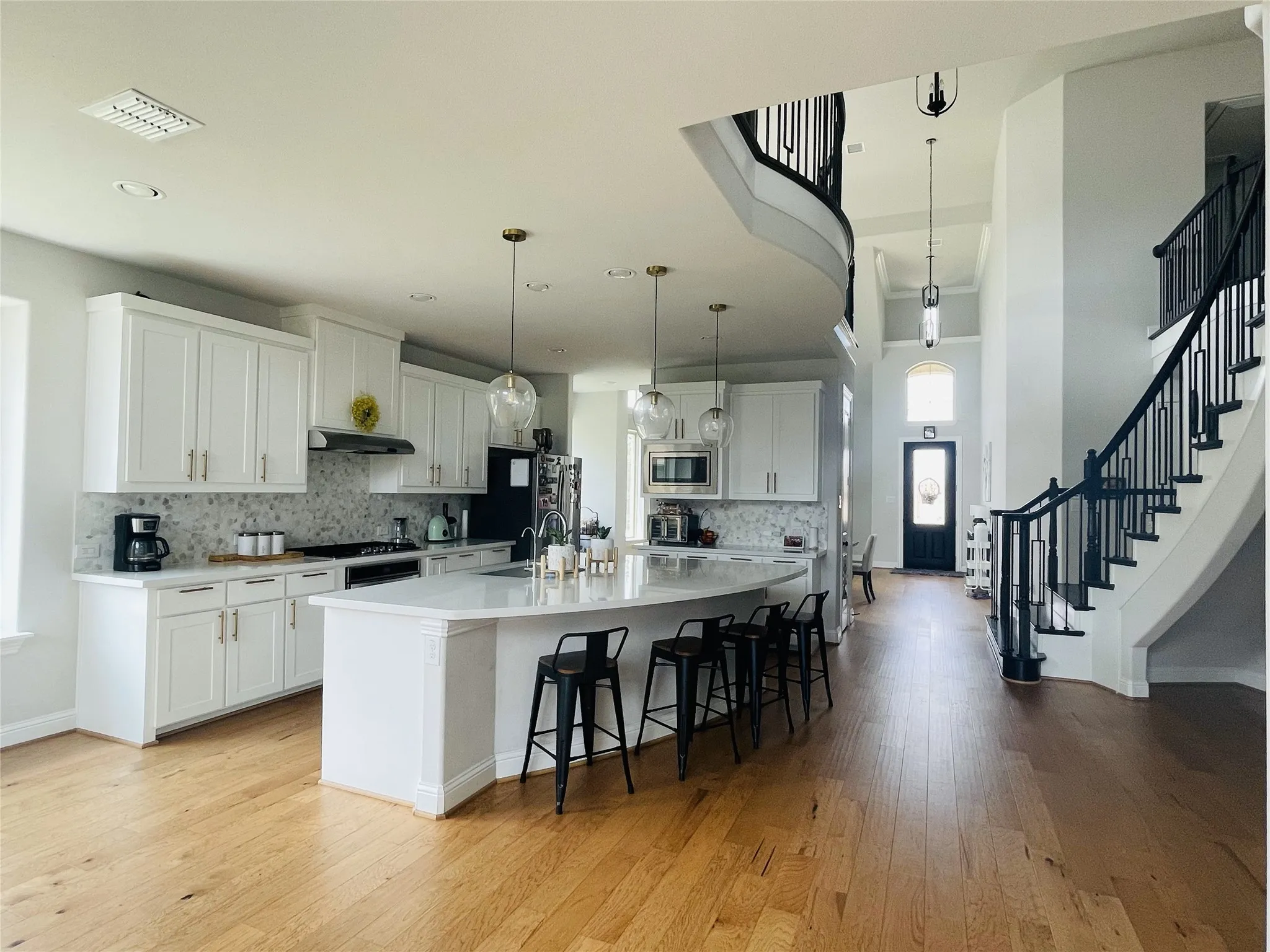 Kitchen with stainless steel microwave, light hardwood / wood-style floors, decorative light fixtures, a kitchen island with sink, and white cabinets