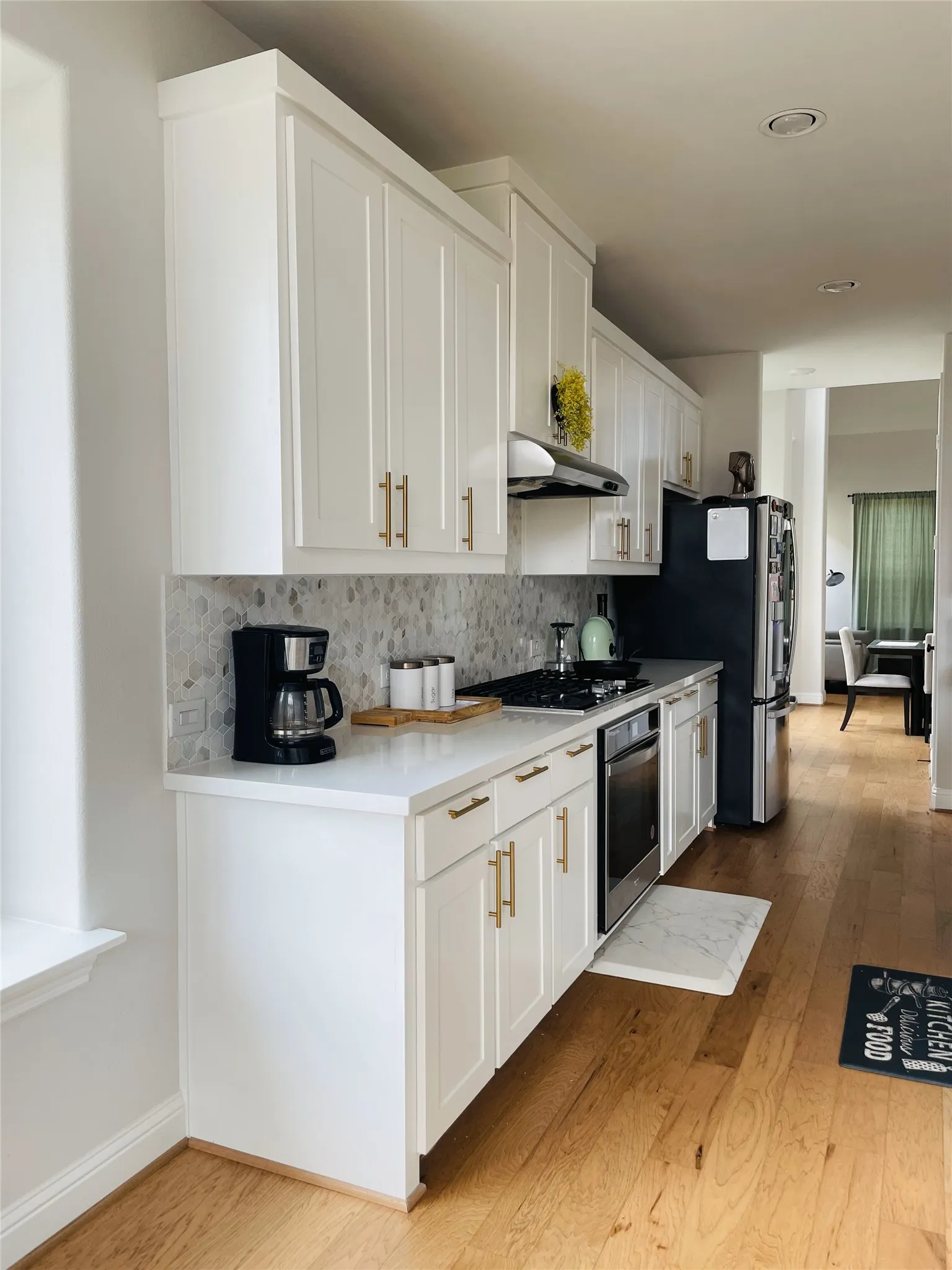 Kitchen with light wood-type flooring, wall oven, backsplash, gas stovetop, and white cabinets
