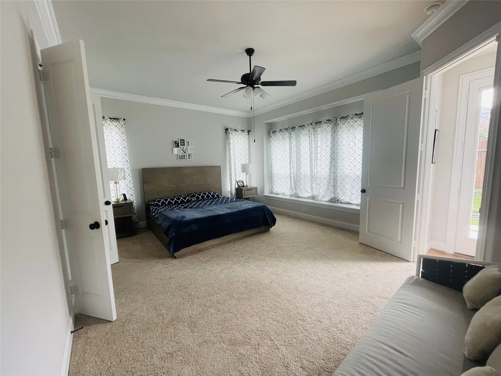 Carpeted bedroom with ceiling fan, ornamental molding, and multiple windows
