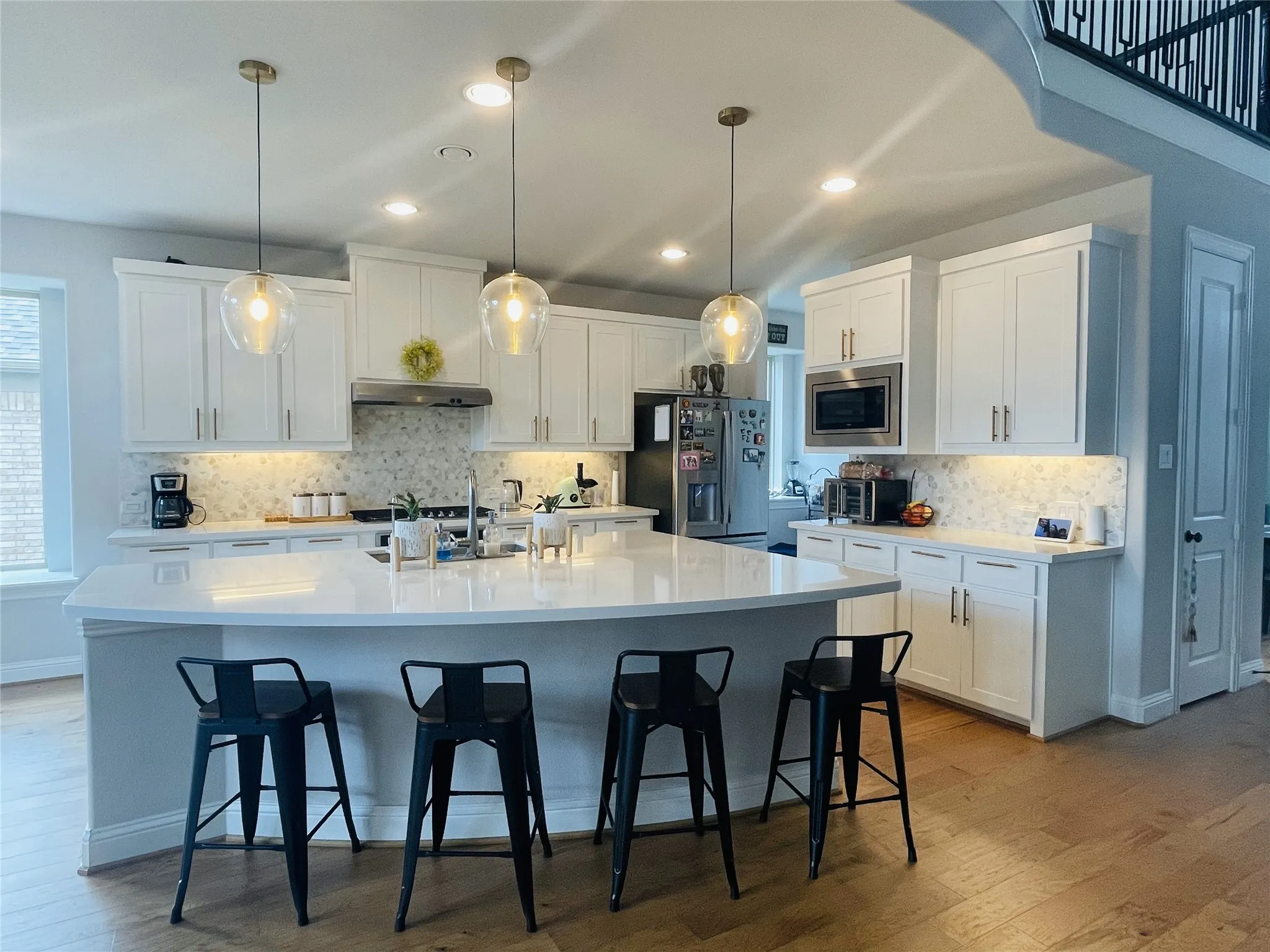 Kitchen with stainless steel appliances, light hardwood / wood-style flooring, range hood, white cabinets, and an island with sink