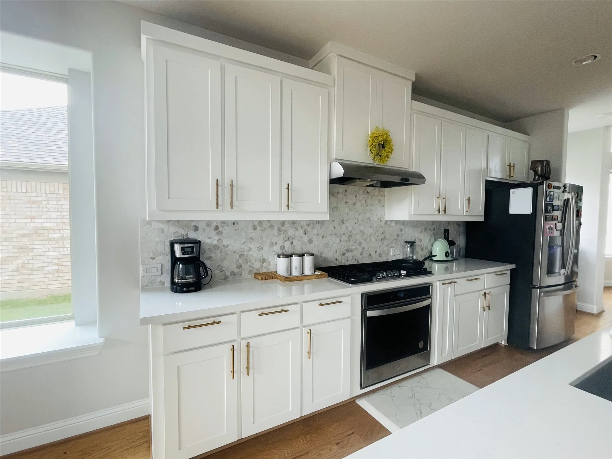 Kitchen featuring white cabinets, decorative backsplash, stainless steel appliances, and hardwood / wood-style floors