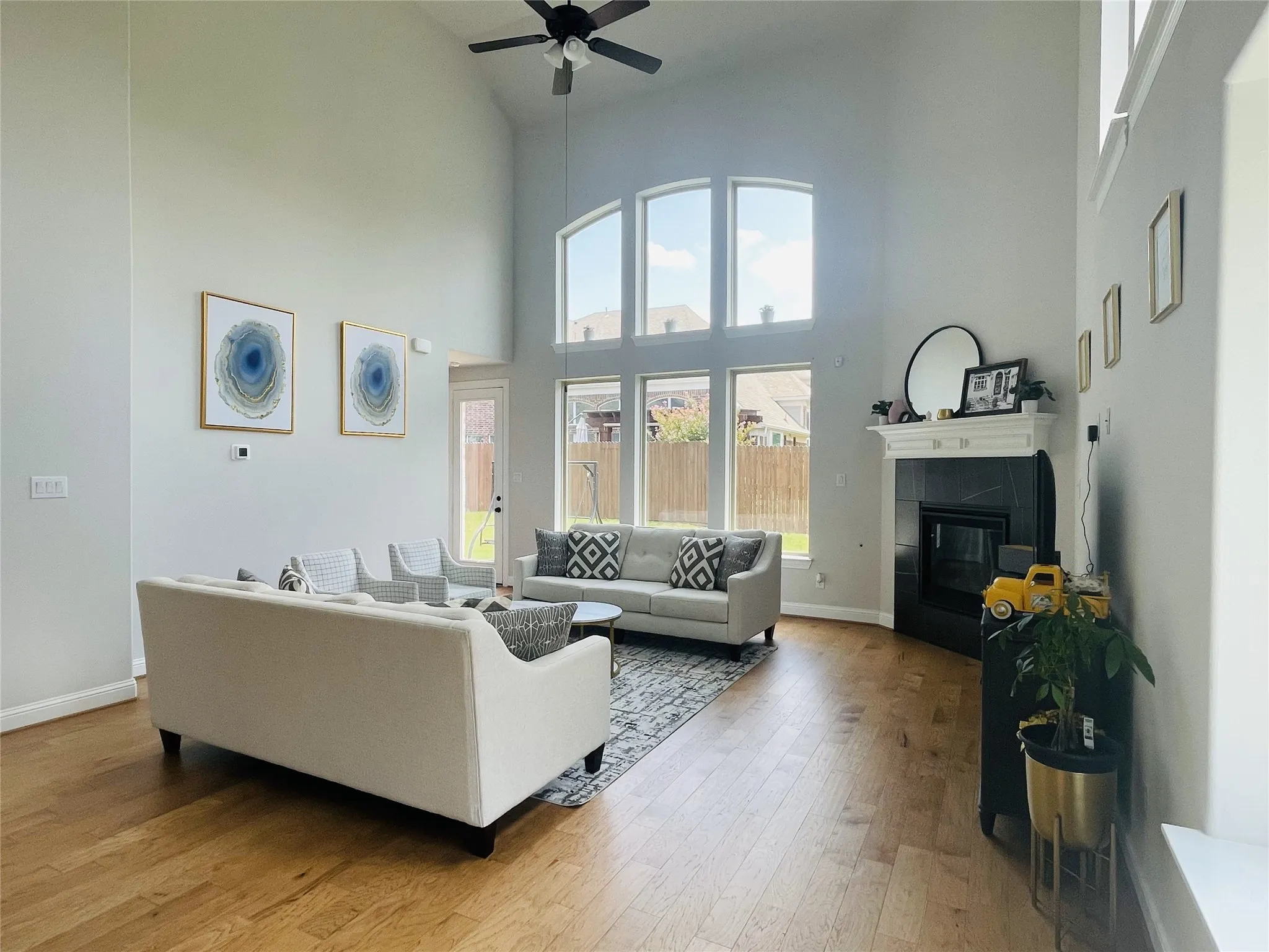 Living room featuring hardwood / wood-style flooring, ceiling fan, a high ceiling, and a tiled fireplace