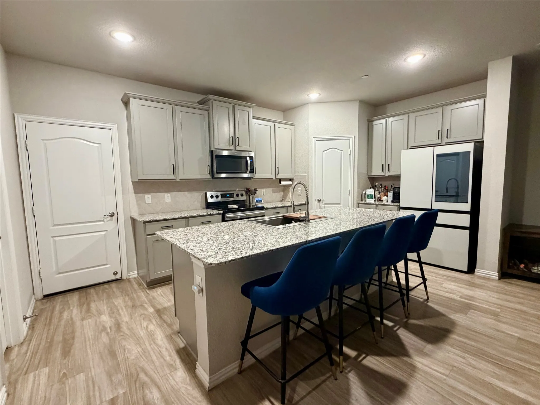 Kitchen featuring a large island with stone countertop, stainless steel appliances, light-toned cabinetry, a subway tile backsplash, and wood-finish flooring