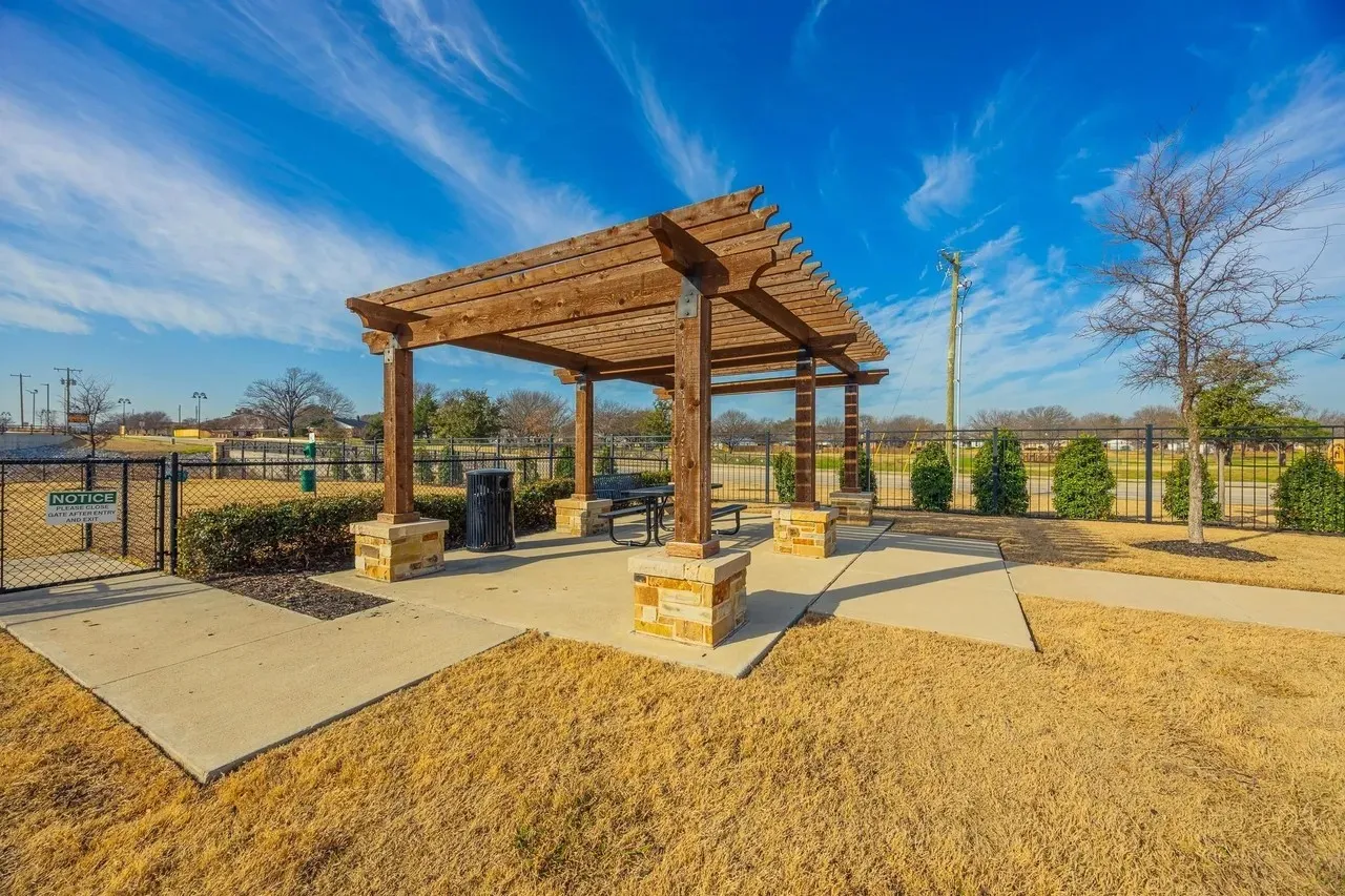 Wood pergola with stone-clad pillars, concrete patio, and fenced perimeter