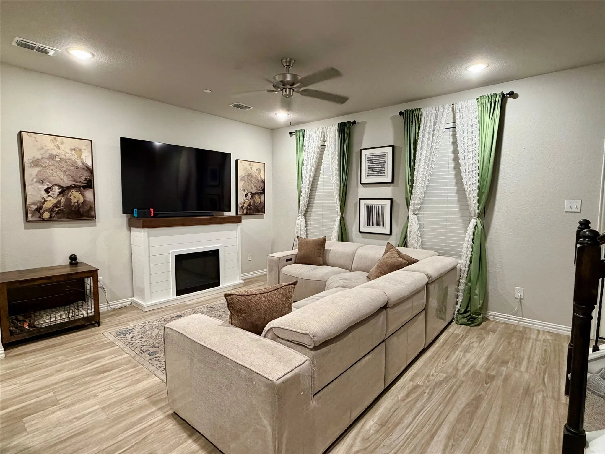 Recessed lighting, wood-finish flooring, ceiling fan, shiplap-detailed fireplace, and multiple windows with blinds