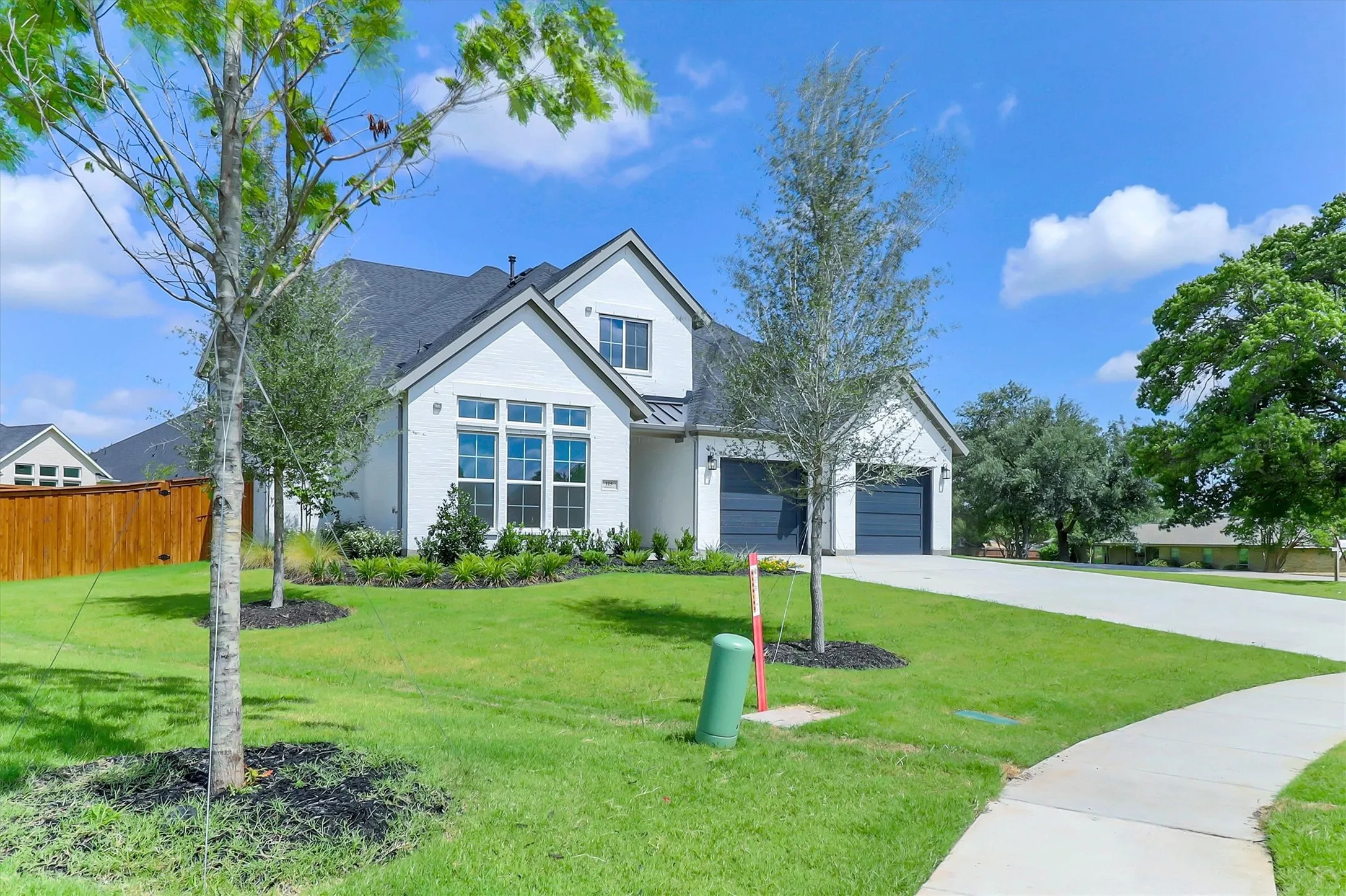 White brick exterior with dark gray roof, multiple gables, attached two-car garage, concrete driveway, and a front yard with mature landscaping