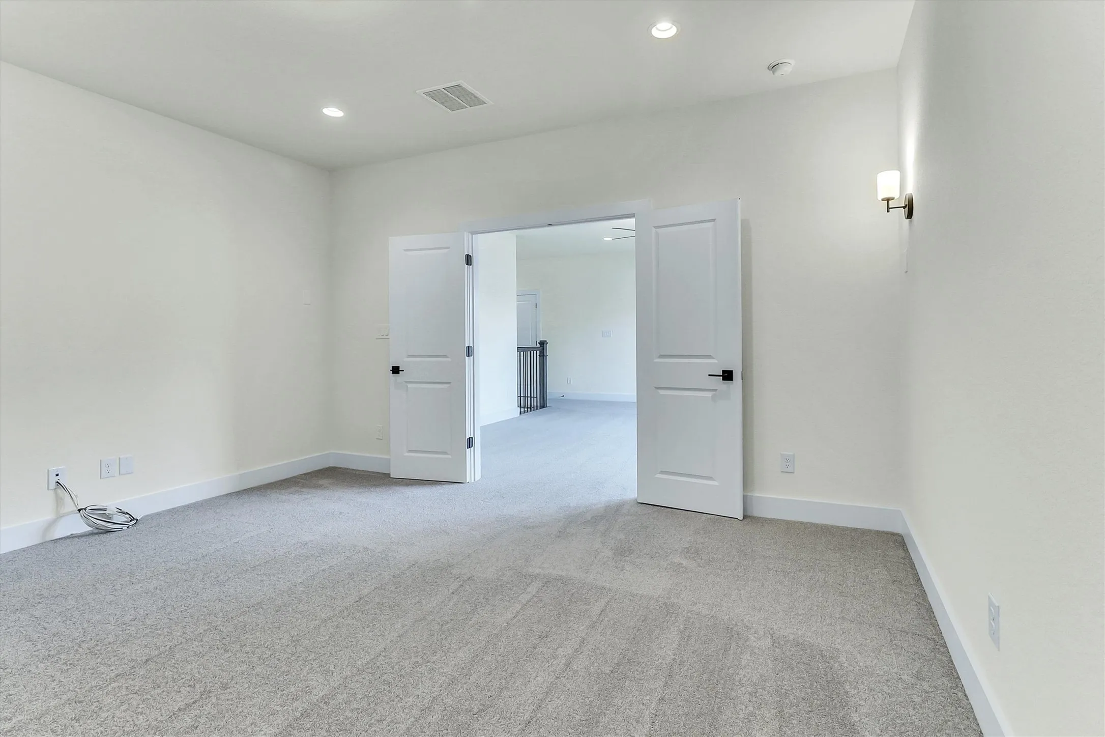 Light gray carpet, recessed ceiling lighting, wall-mounted sconce, and white paneled double doors