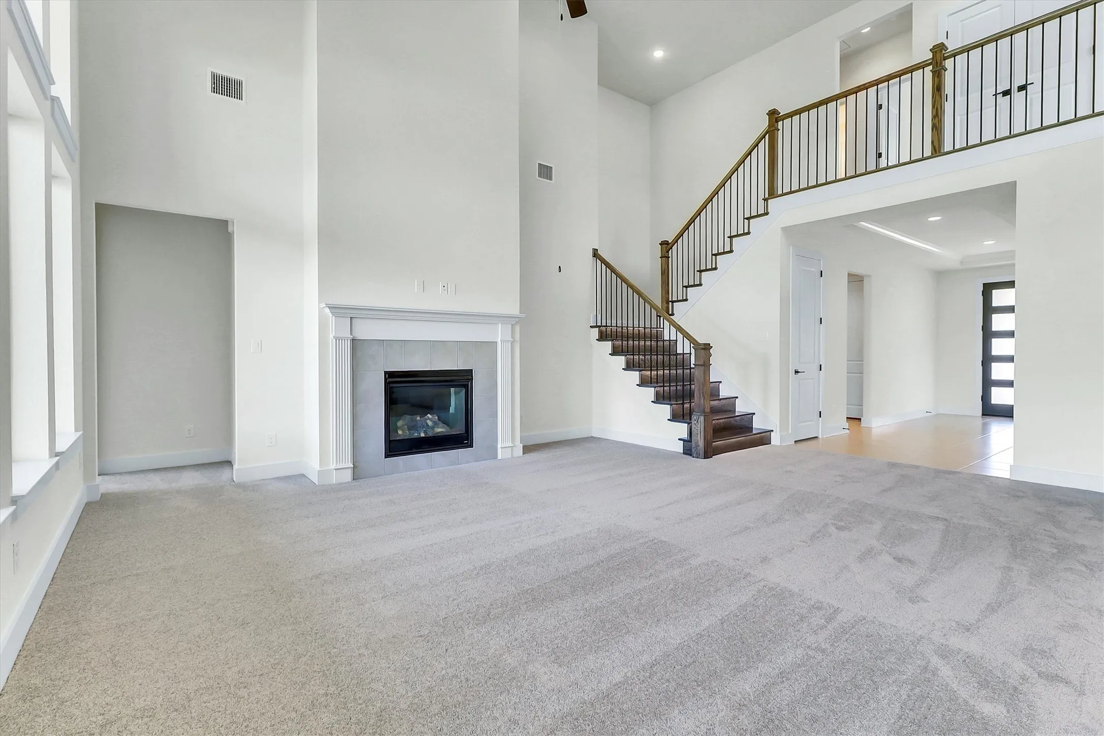 Two-story living area featuring a fireplace with a light-toned surround, a grand staircase with dark wood treads and wrought iron balusters, and a carpeted floor
