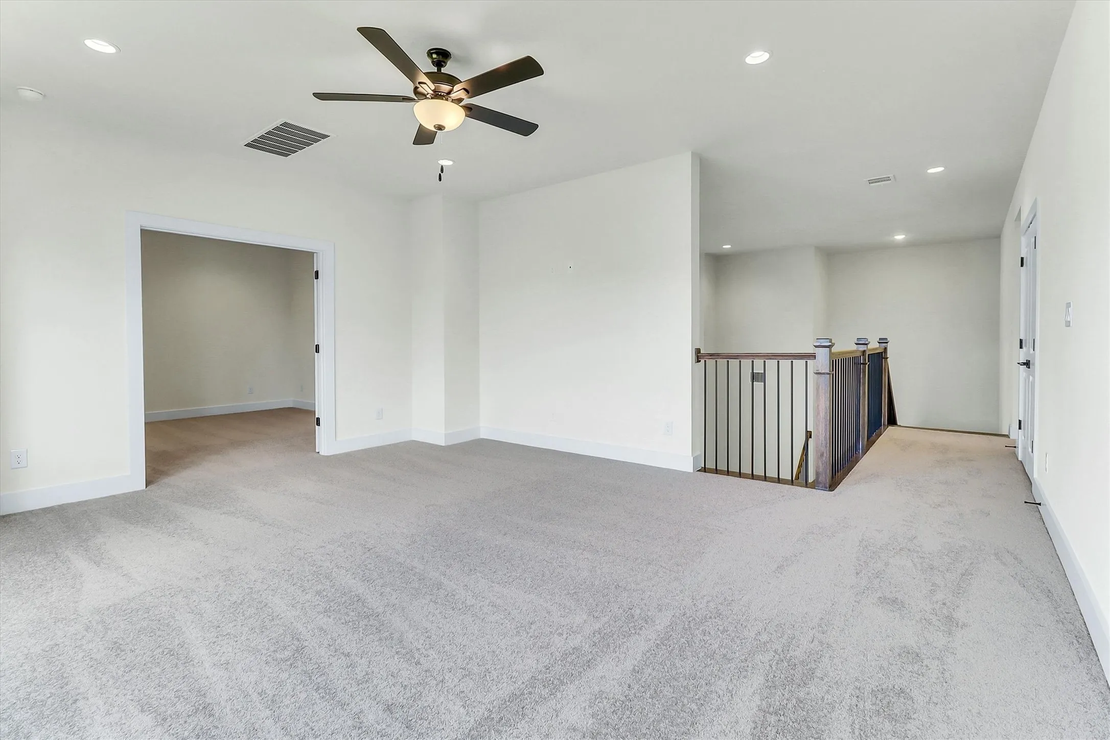 Recessed lighting, ceiling fan, neutral wall paint, light-colored carpeting, and a wood and metal staircase railing