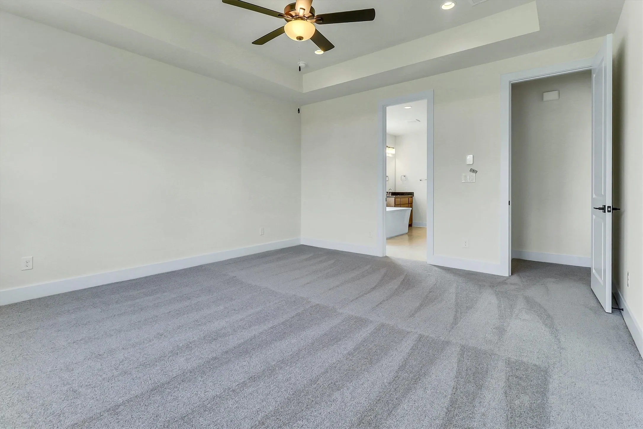 Spacious room featuring gray carpeting, tray ceiling, recessed lighting, and a ceiling fan with integrated light