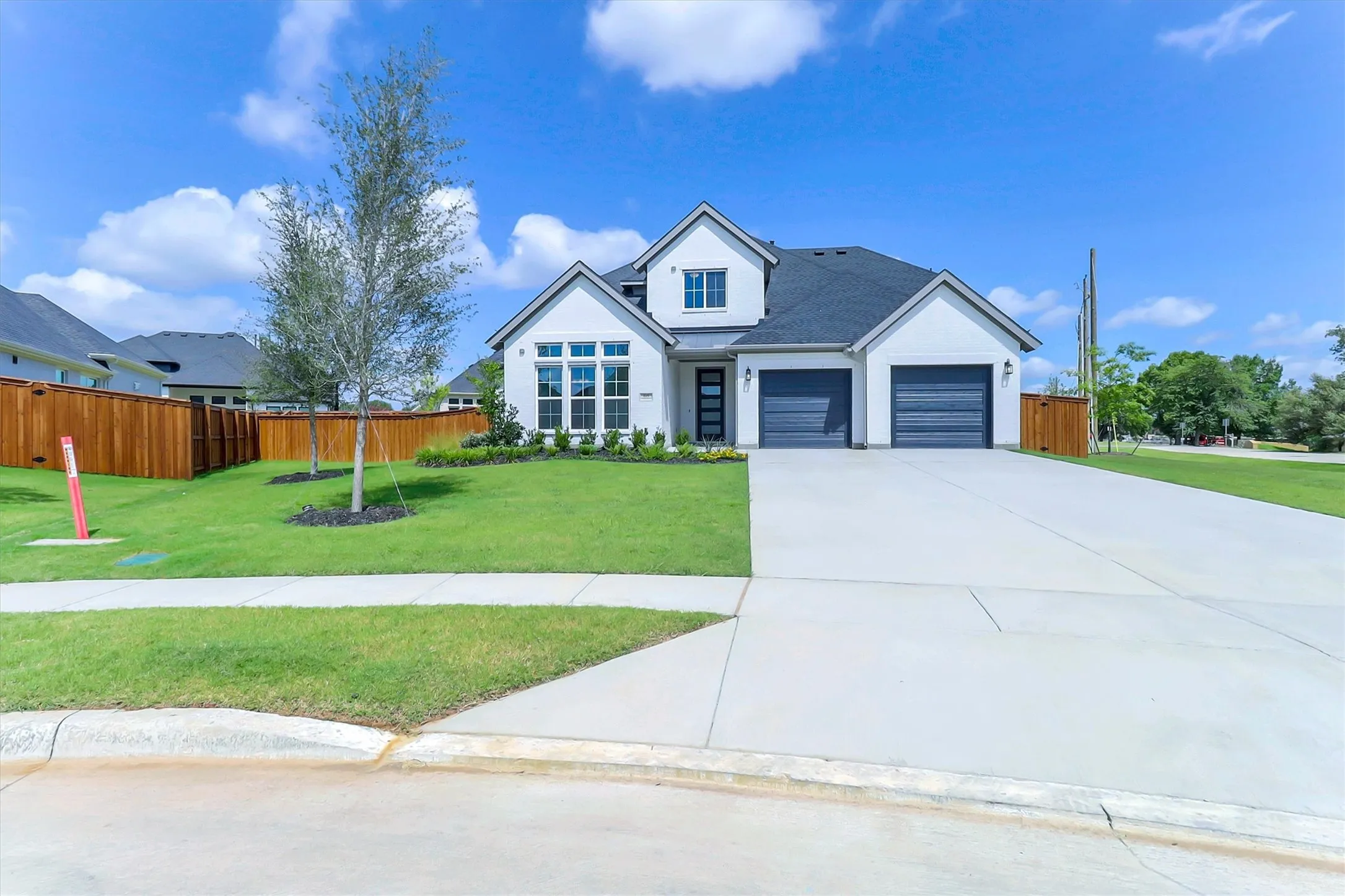 White exterior with dark roof, two-car garage, manicured lawn, and concrete driveway