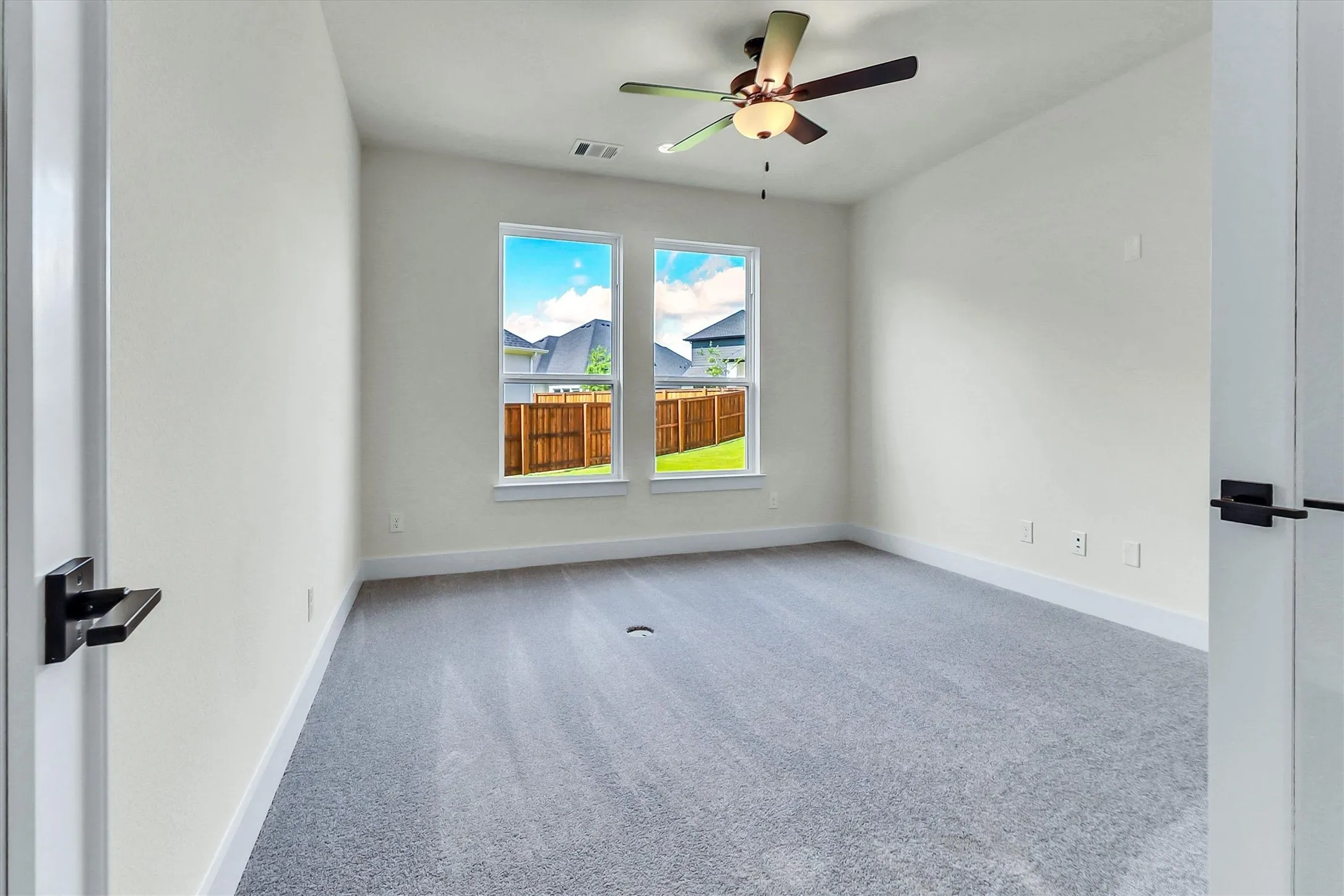 Carpeted room featuring two windows, a ceiling fan with integrated lighting, and a neutral color palette