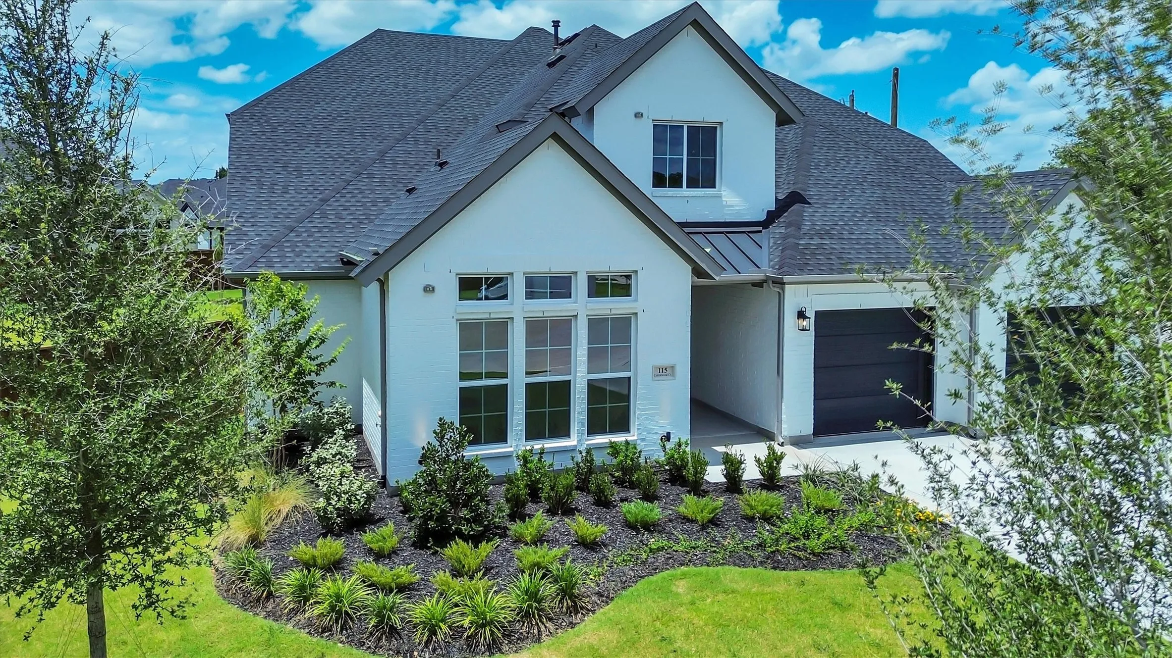 White exterior with dark gray accents, a two-car garage, and landscaped front yard