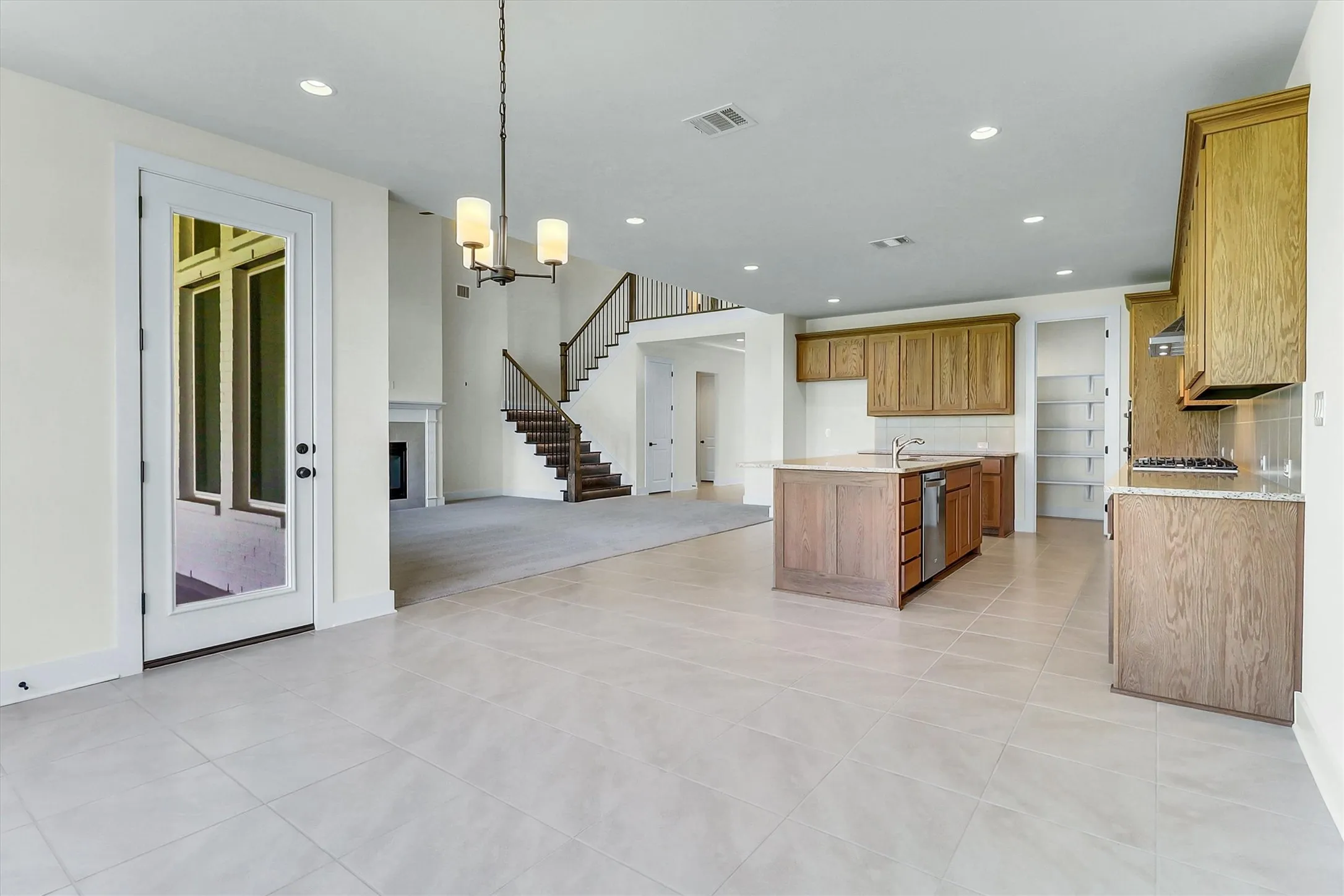 Light-toned tile flooring, recessed lighting, wood-finish cabinetry, built-in shelving, and a prominent staircase with dark wood-finish treads