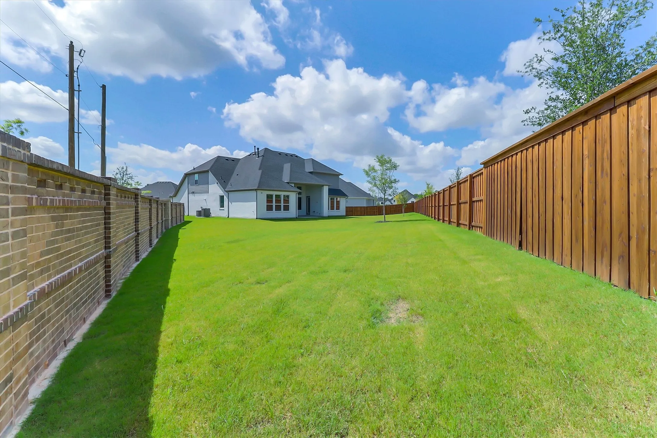 Expansive green lawn, brick perimeter wall, and a wood privacy fence enclose the rear of the property