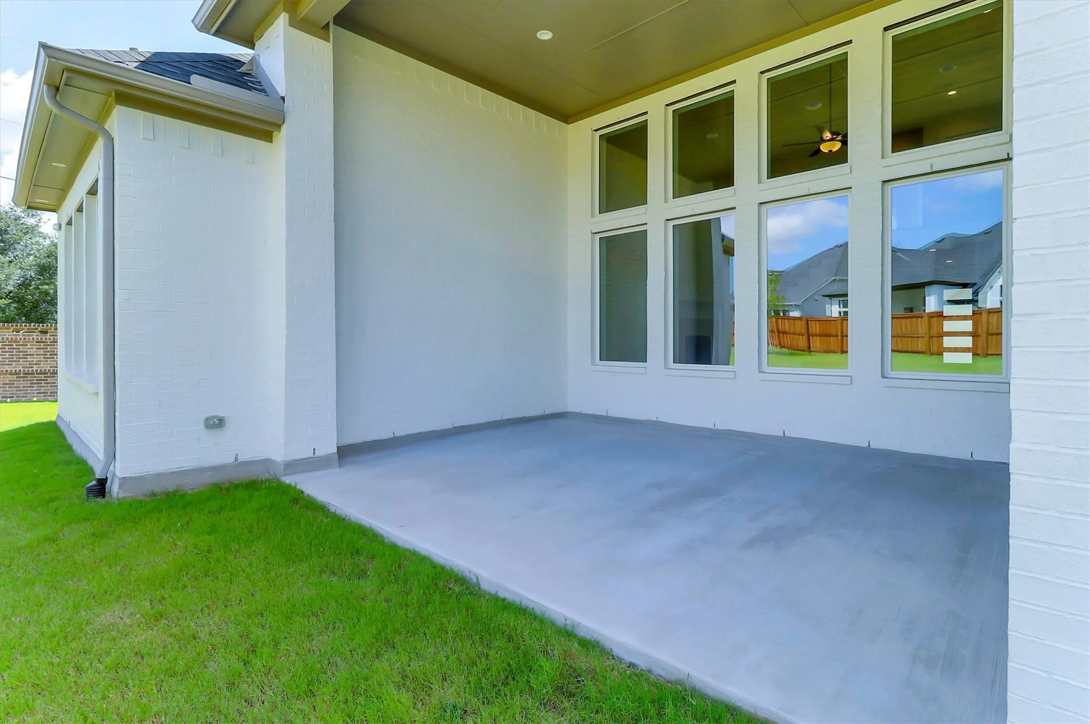 Covered outdoor patio with a concrete surface, white brick exterior, and multi-pane windows