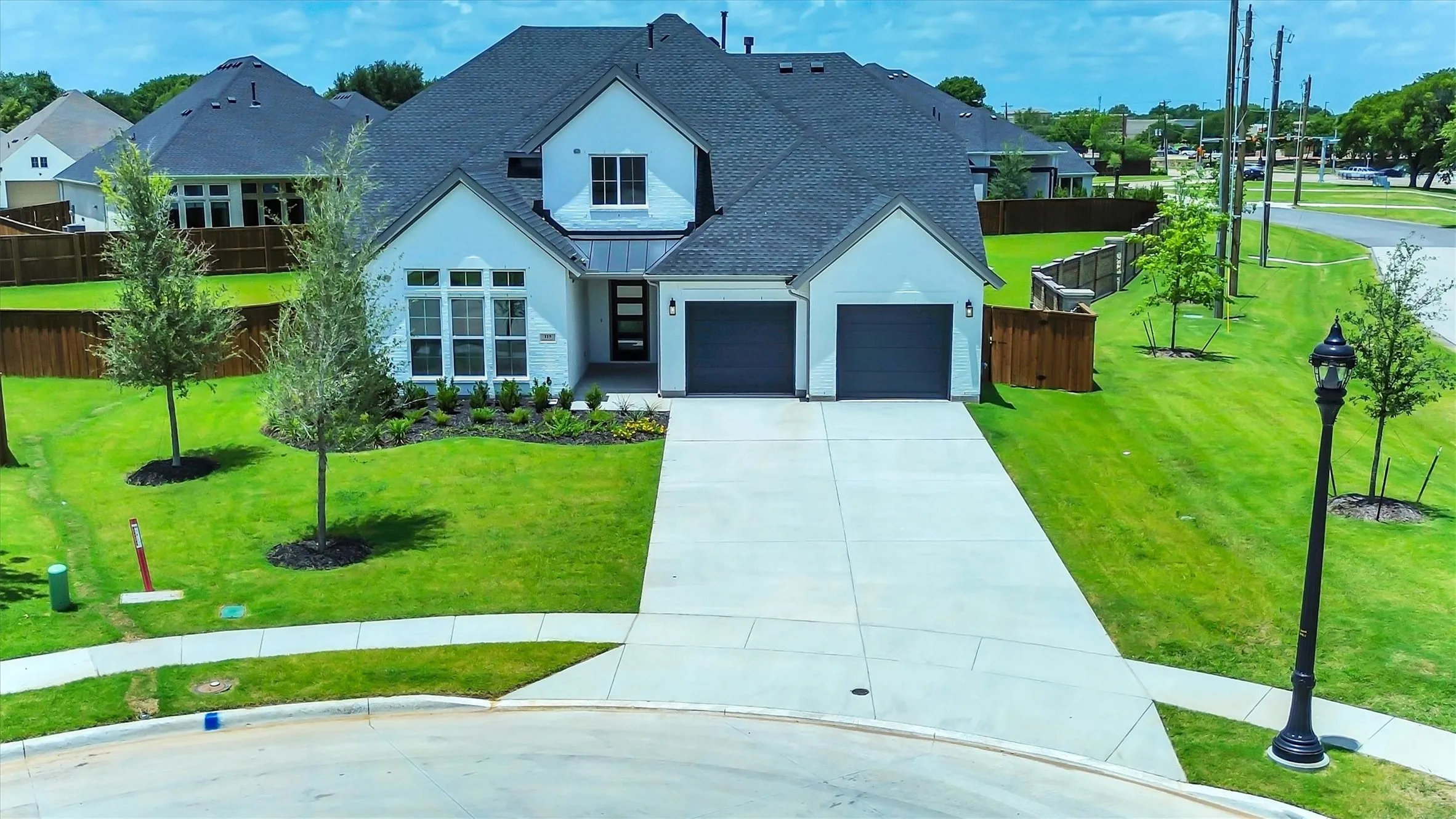 Contemporary white exterior with dark gray roof, two-car garage, manicured lawn with mature trees, and a concrete driveway