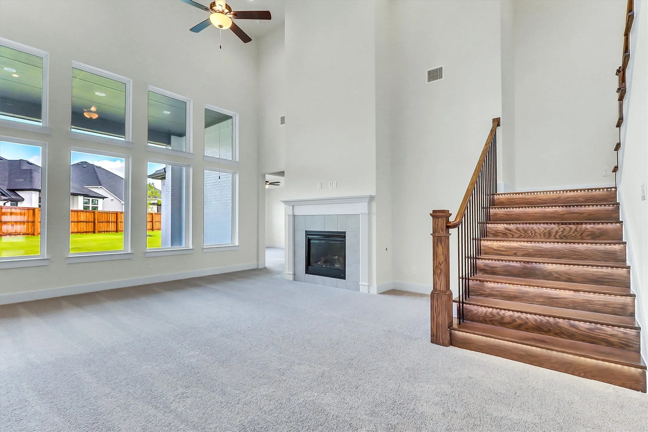Two-story living area featuring a fireplace with a mantel, a ceiling fan, a carpeted floor, and a wood staircase with metal balusters