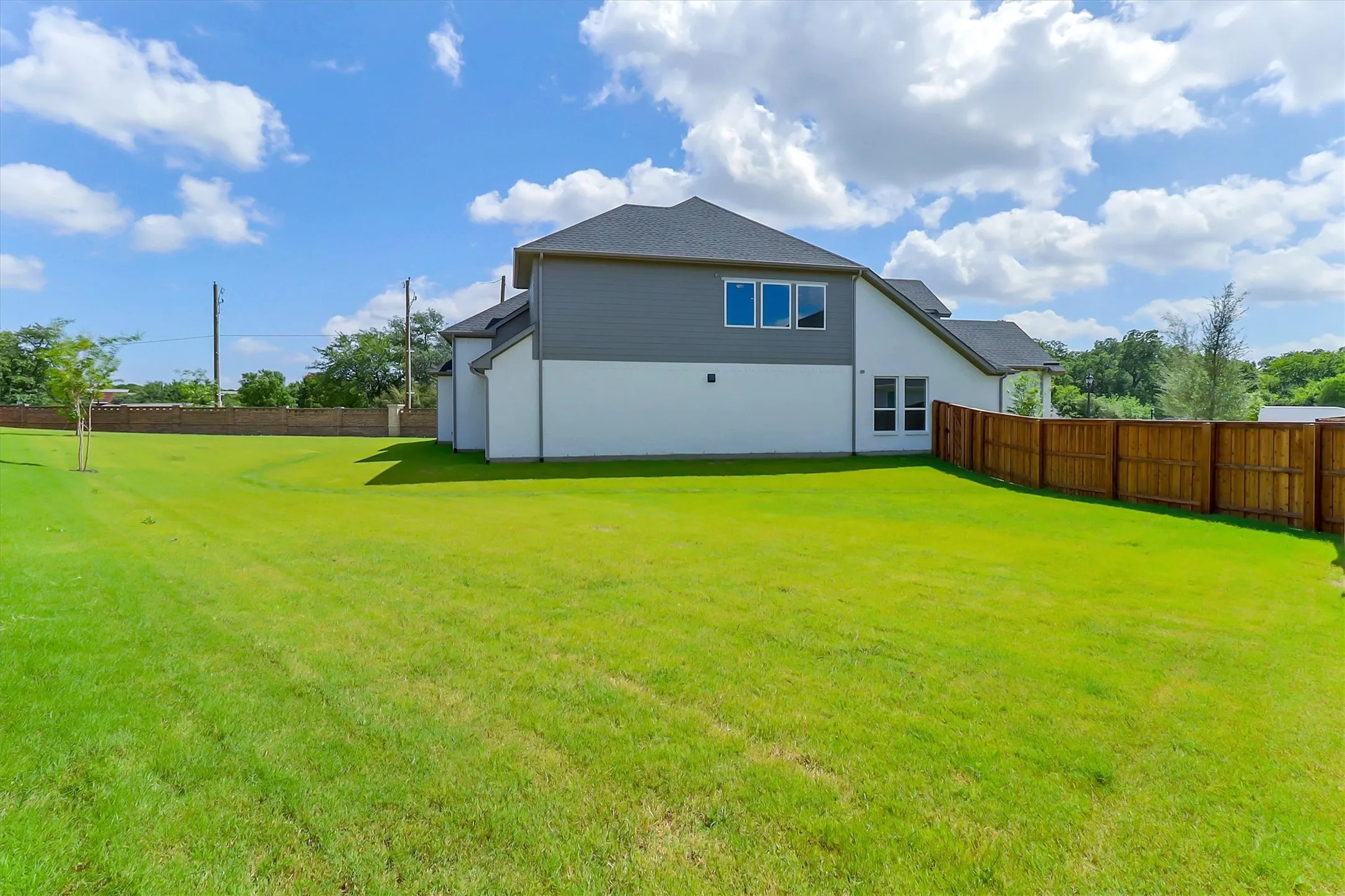 Expansive green lawn, dark shingle roofing, horizontal siding, white exterior walls, and a wood privacy fence