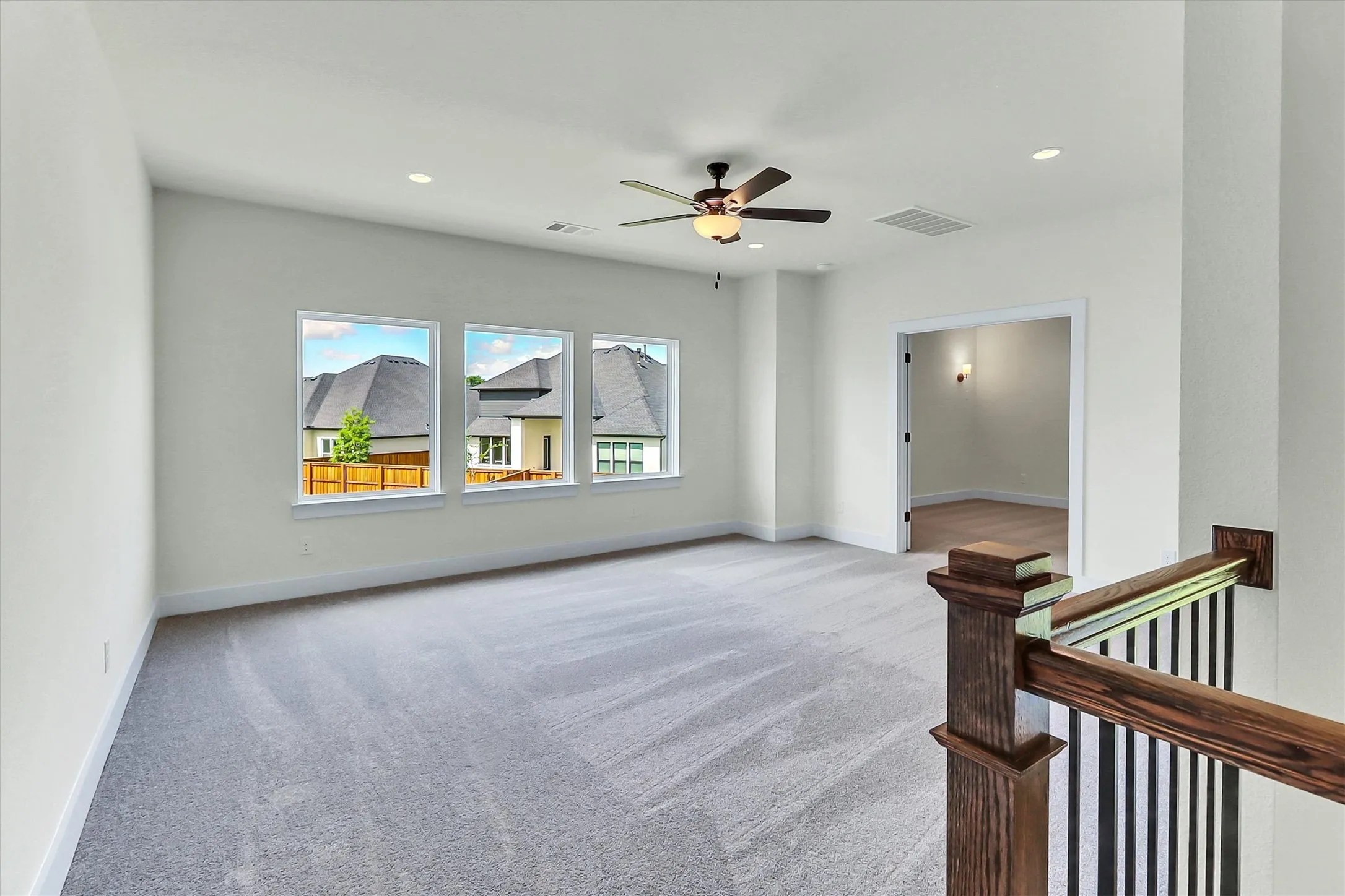 Light grey carpeting with recessed lighting, a ceiling fan, and three large windows