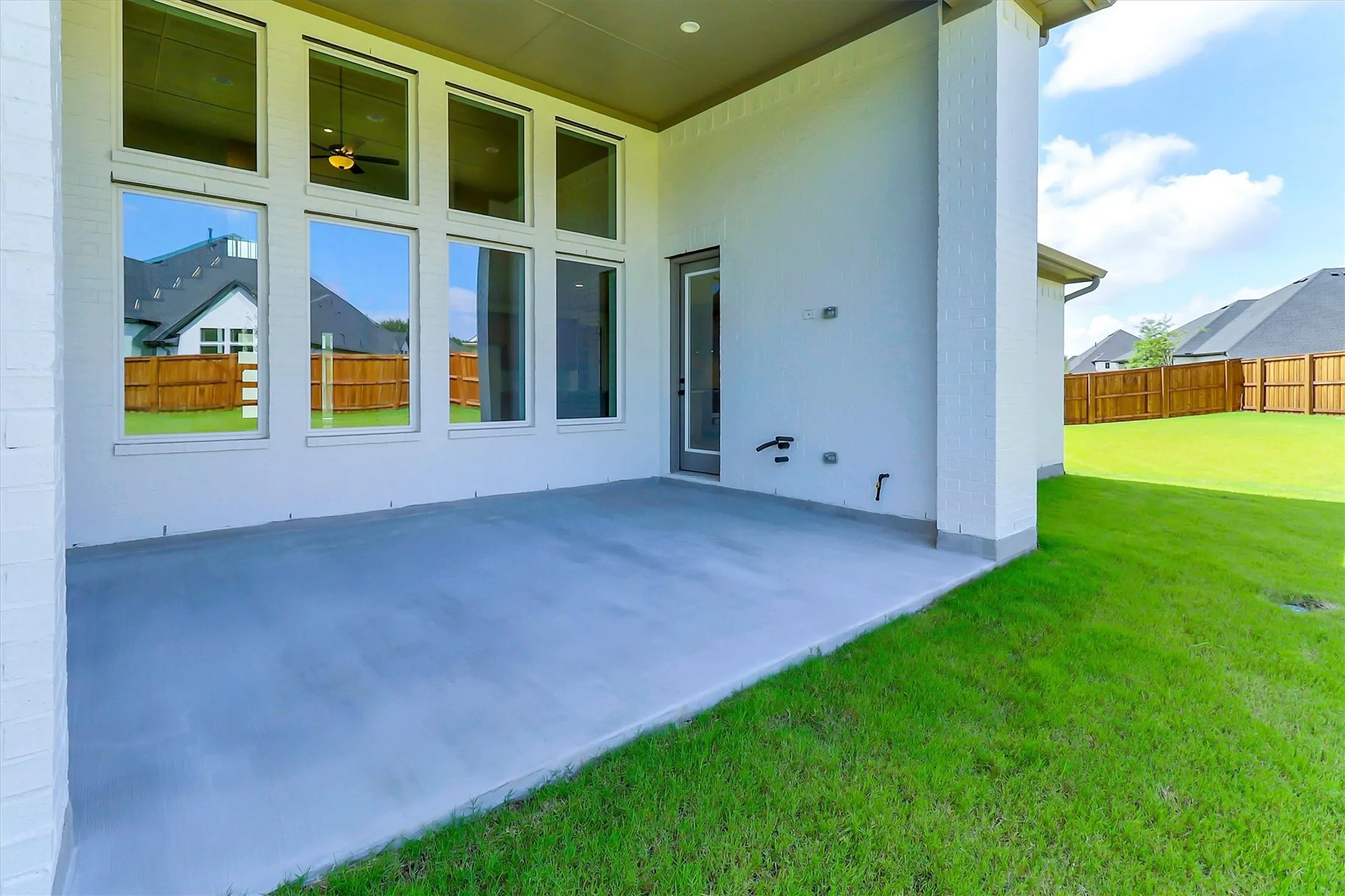 Expansive concrete patio with a full-light glass door, large transom windows, and a manicured lawn