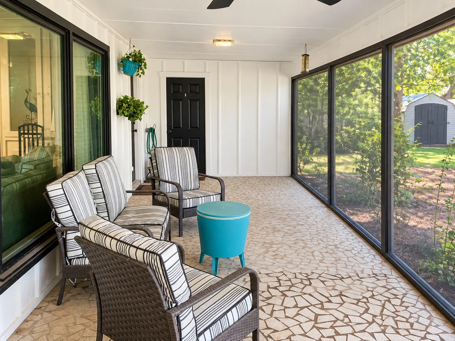 Enclosed patio featuring mosaic-style flooring, white paneling, black framed windows, and a black paneled door