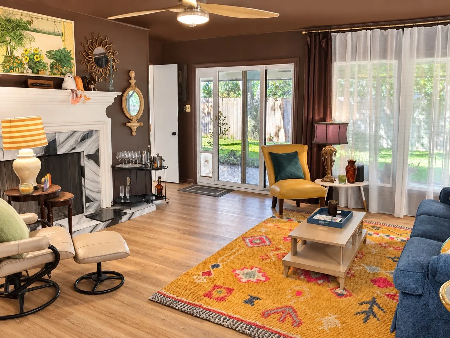 Wood-finish flooring throughout, a fireplace with a black and white marble-look surround, and a ceiling fan with integrated lighting