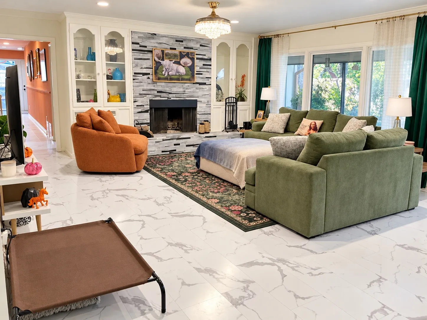 Spacious living area featuring white marble-look flooring, a stone-clad fireplace, built-in cabinetry with glass doors, a decorative ceiling fixture, and large windows