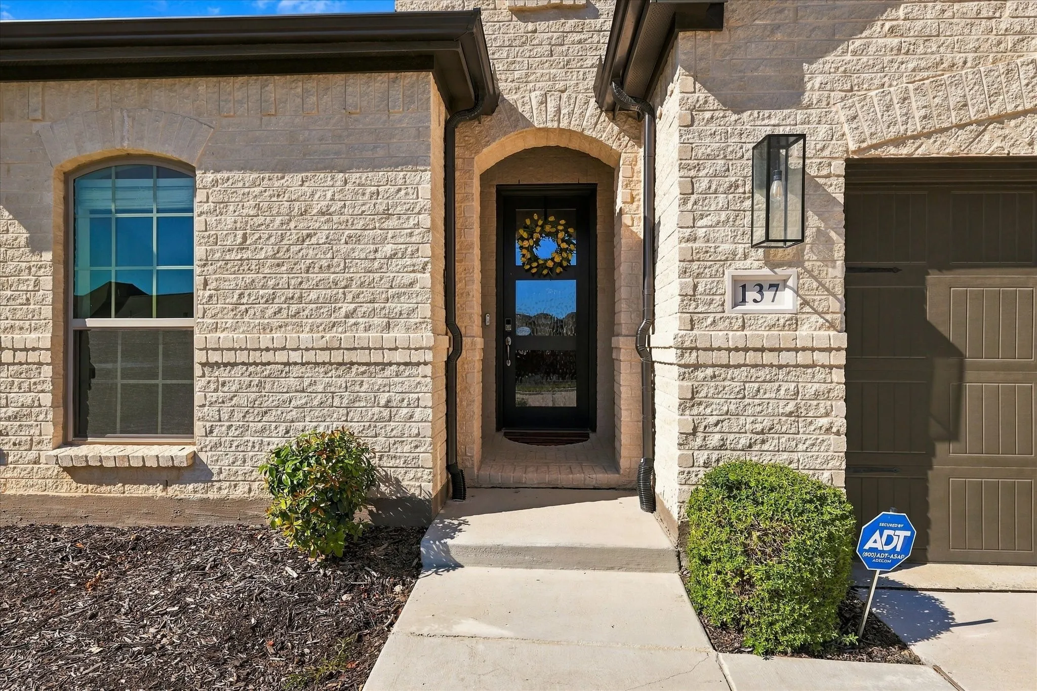 Light-colored brick exterior with arched entryway and a contrasting dark paneled garage door