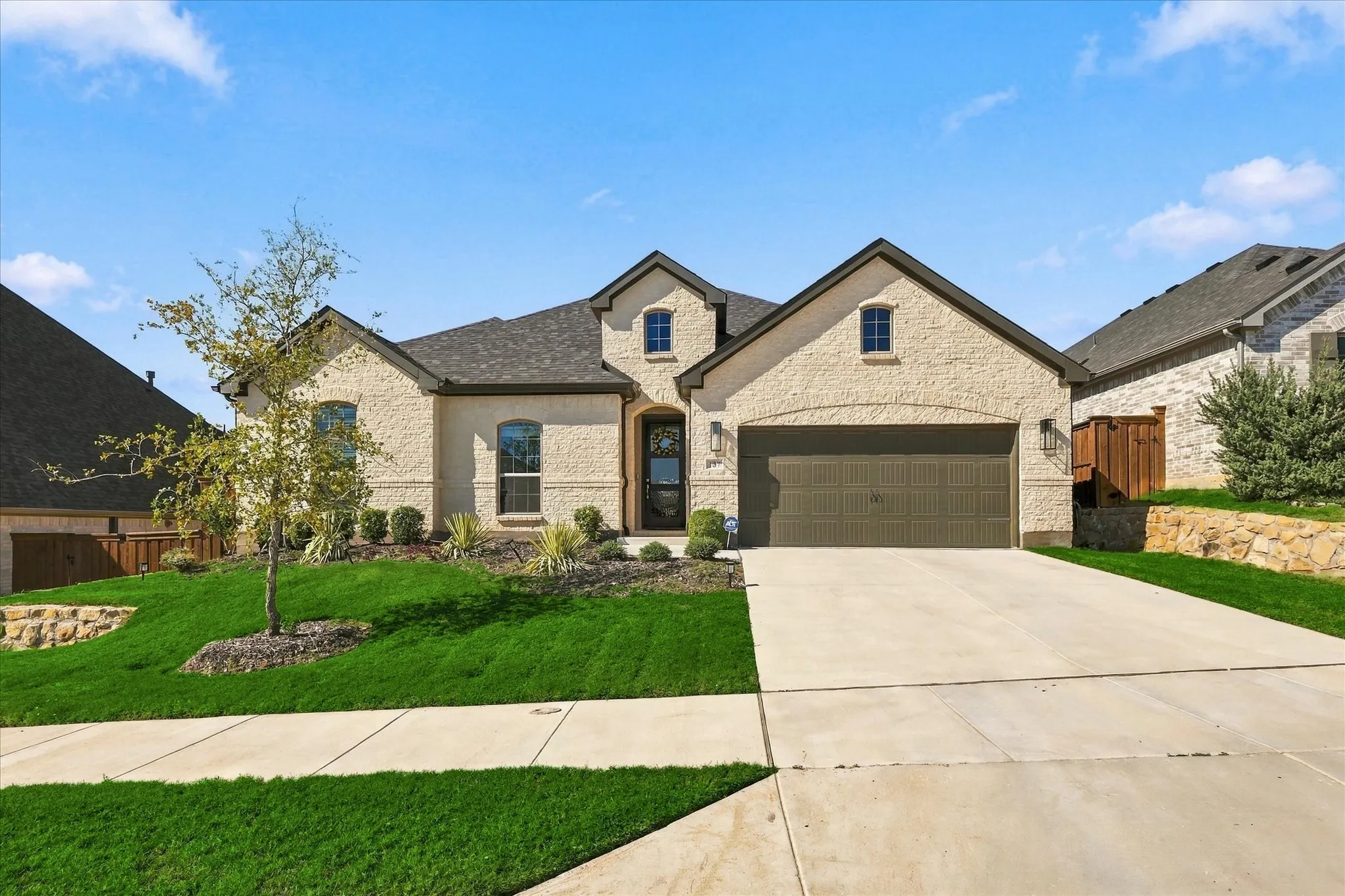 Stucco exterior with stone accents, attached two-car garage, concrete driveway, and landscaped front yard with a retaining wall
