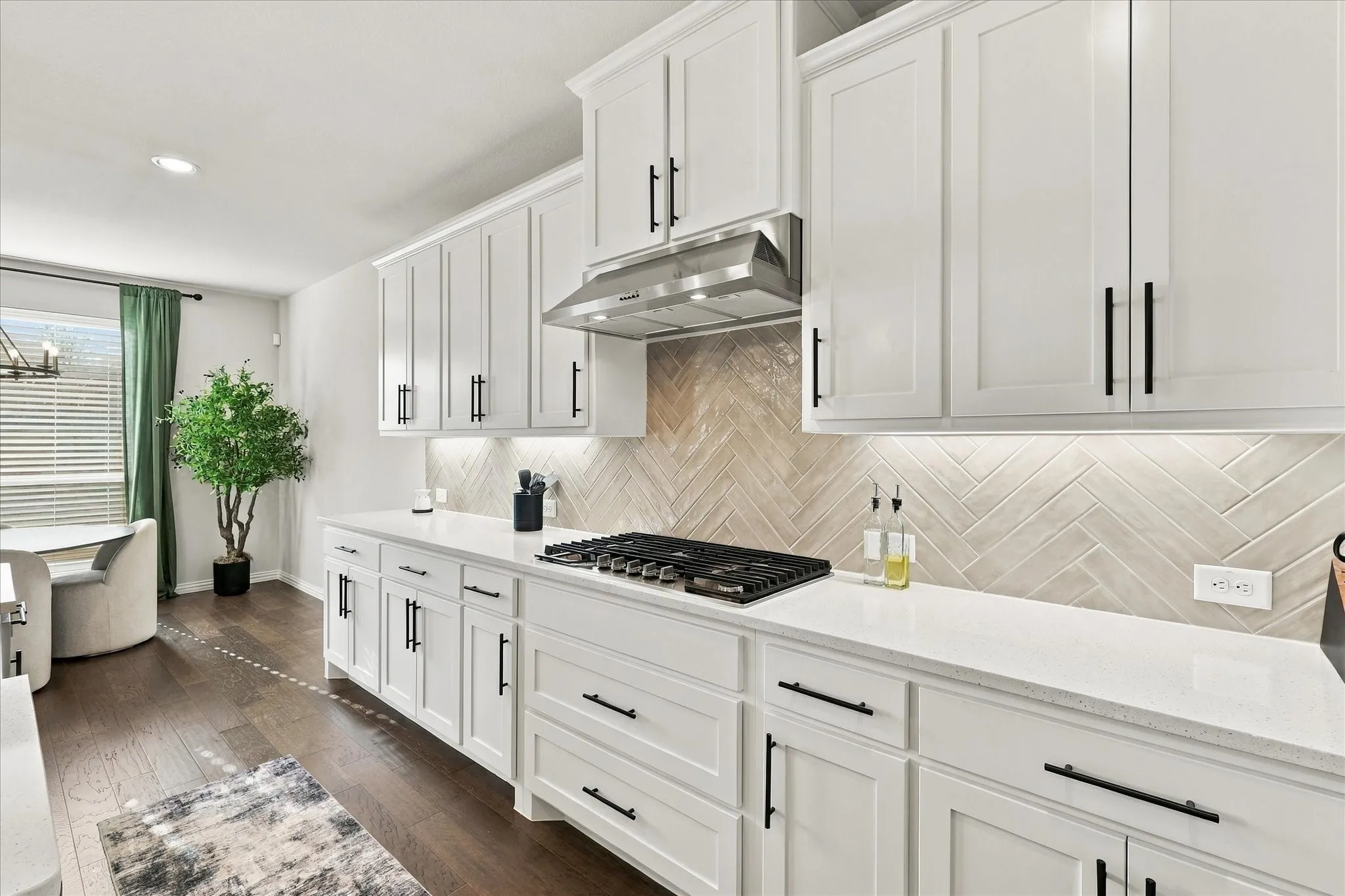 White shaker cabinetry with matte black hardware, quartz countertops, herringbone pattern tile backsplash, stainless steel range hood, and wood-finish flooring