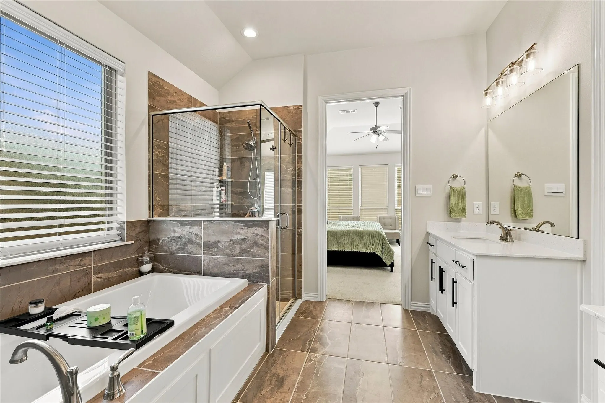 Spacious bathroom featuring a white vanity with under-sink storage, a large mirror, a separate tub, a glass-enclosed shower, and tile flooring