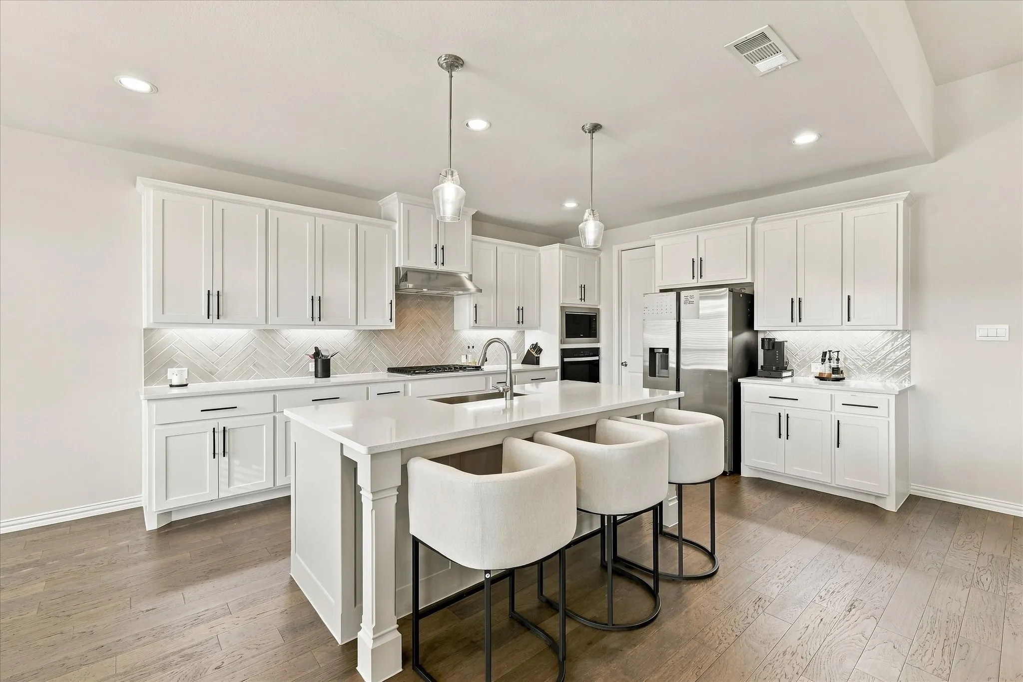 Bright kitchen featuring white shaker cabinetry, an island with solid surface countertops, stainless steel appliances, wood-finish flooring, and recessed lighting