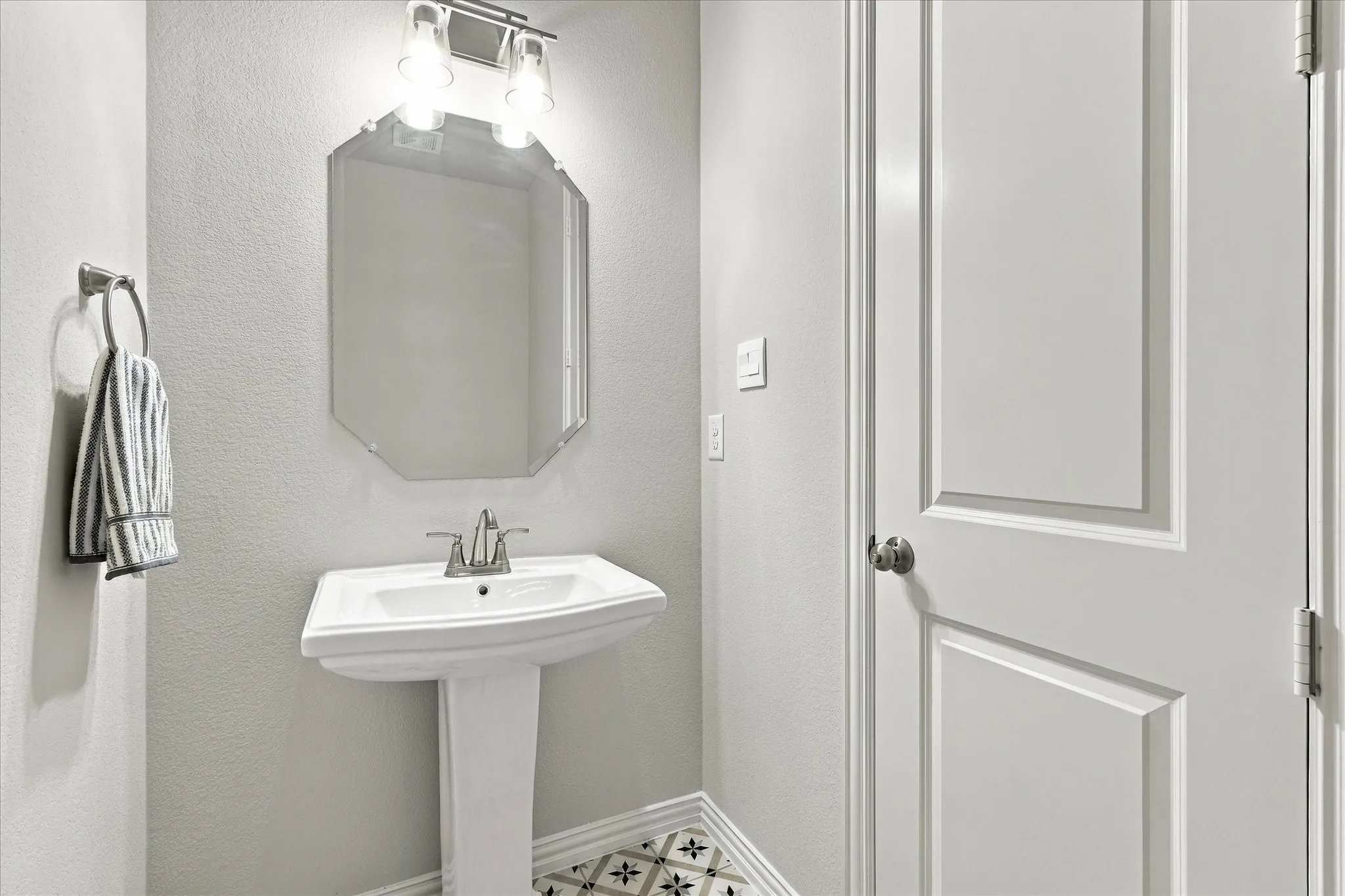 Pedestal sink with chrome faucet, octagonal wall mirror, and decorative patterned floor tile