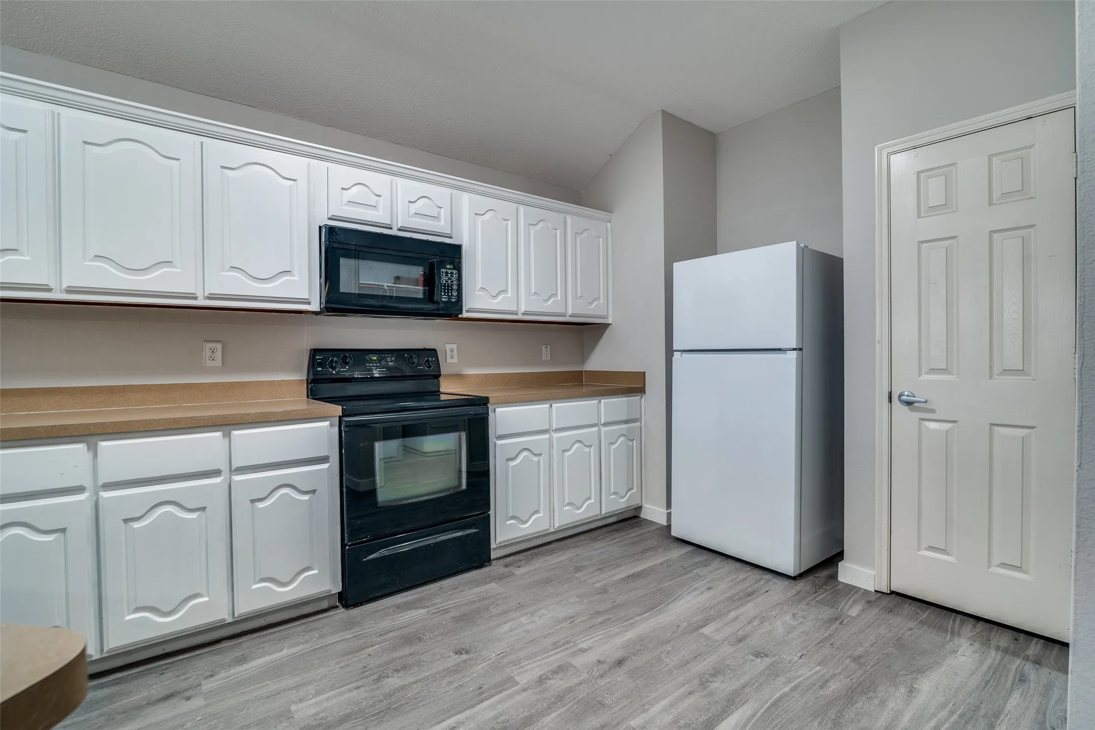 Kitchen featuring white cabinetry with arch details, light-toned countertops, wood-finish flooring, a black range, and an over-the-range microwave