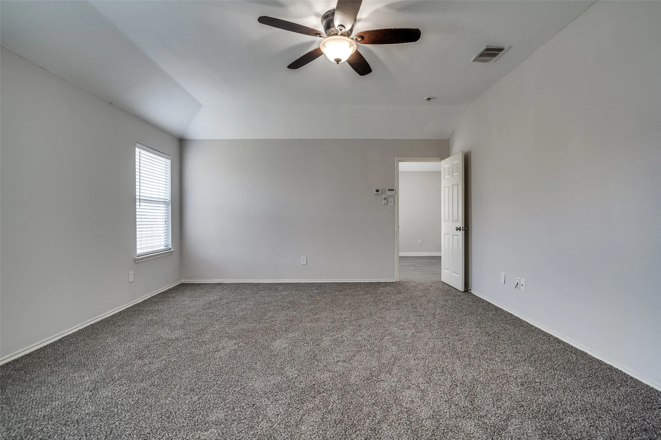 Neutral gray walls, vaulted ceiling, ceiling fan with integrated lighting, window with blinds, and gray carpet flooring