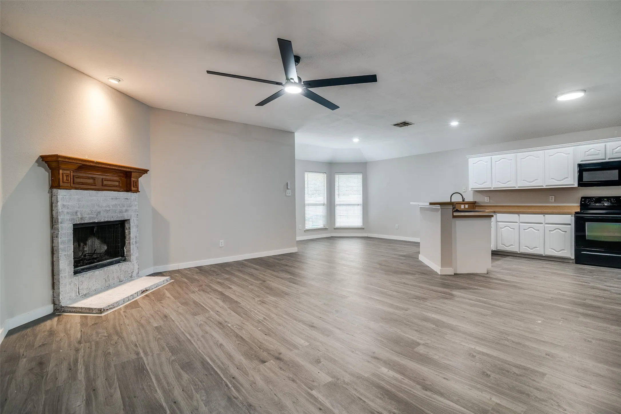 Wood-finish flooring throughout, ceiling fan with integrated lighting, built-in fireplace with wood mantel, kitchen island with sink, and white cabinetry