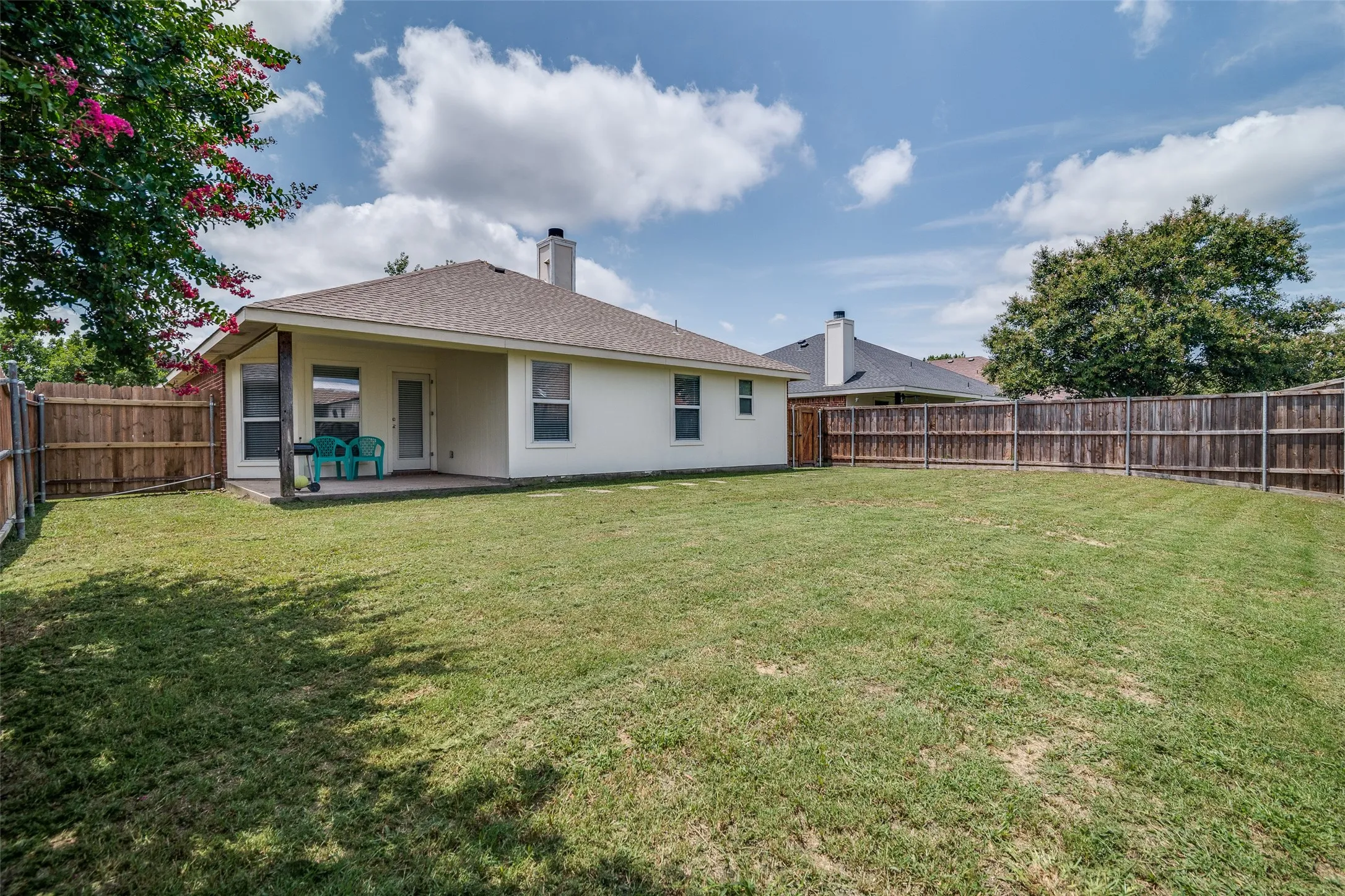 Expansive backyard with a manicured lawn, full wood fencing, and a covered concrete patio