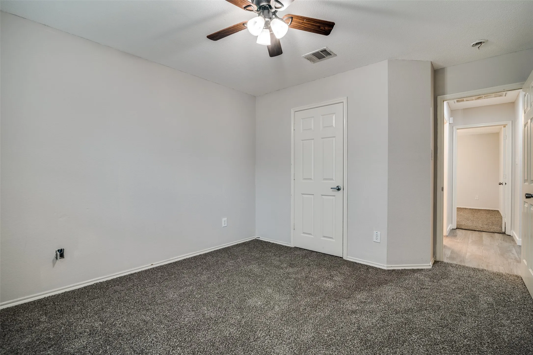 Wall-to-wall carpeting with light gray walls, a white paneled door, and a ceiling fan with wood-finish blades