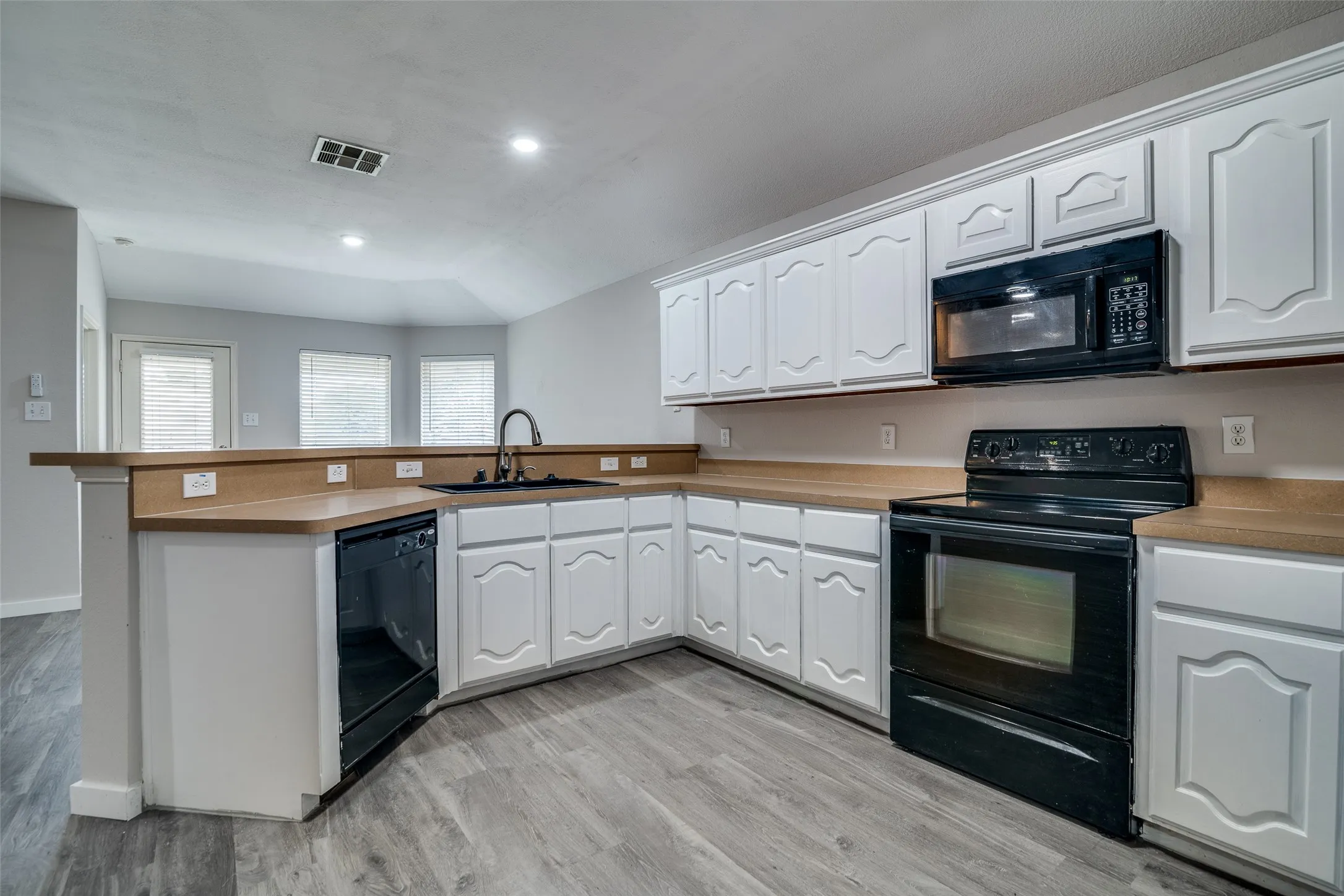 Kitchen featuring white cabinetry, light countertops, black appliances, a black sink with a gooseneck faucet, and wood-finish flooring