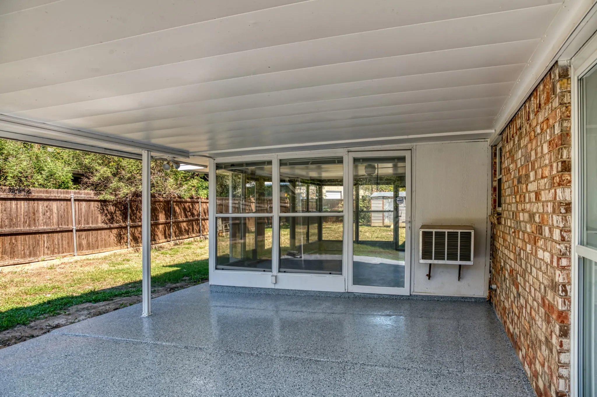 Covered patio with a speckled concrete finish, offering direct access to an enclosed sunroom through a glass-paneled door