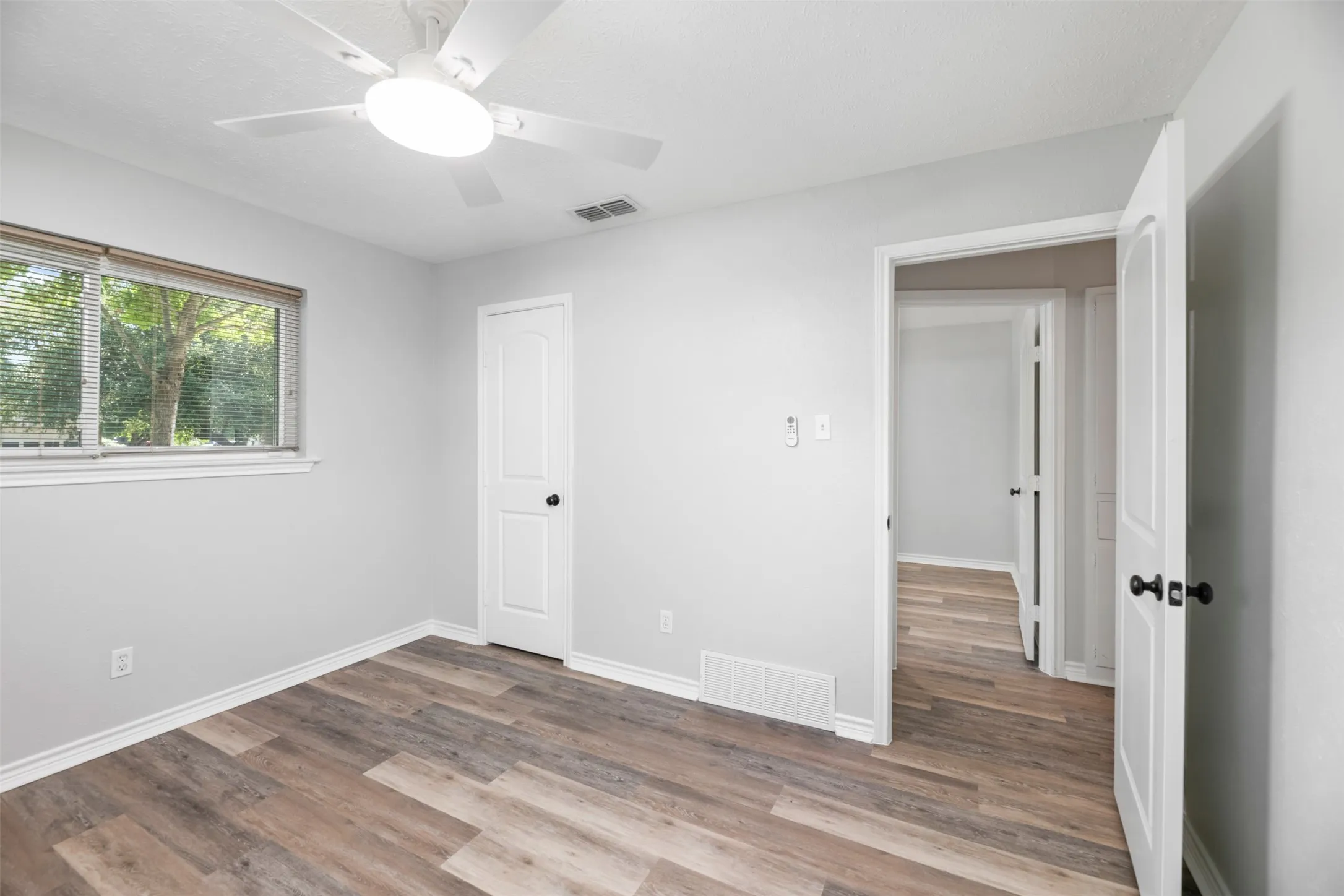 Wood-finish flooring, light gray wall tones, a ceiling fan with integrated lighting, and a window with blinds
