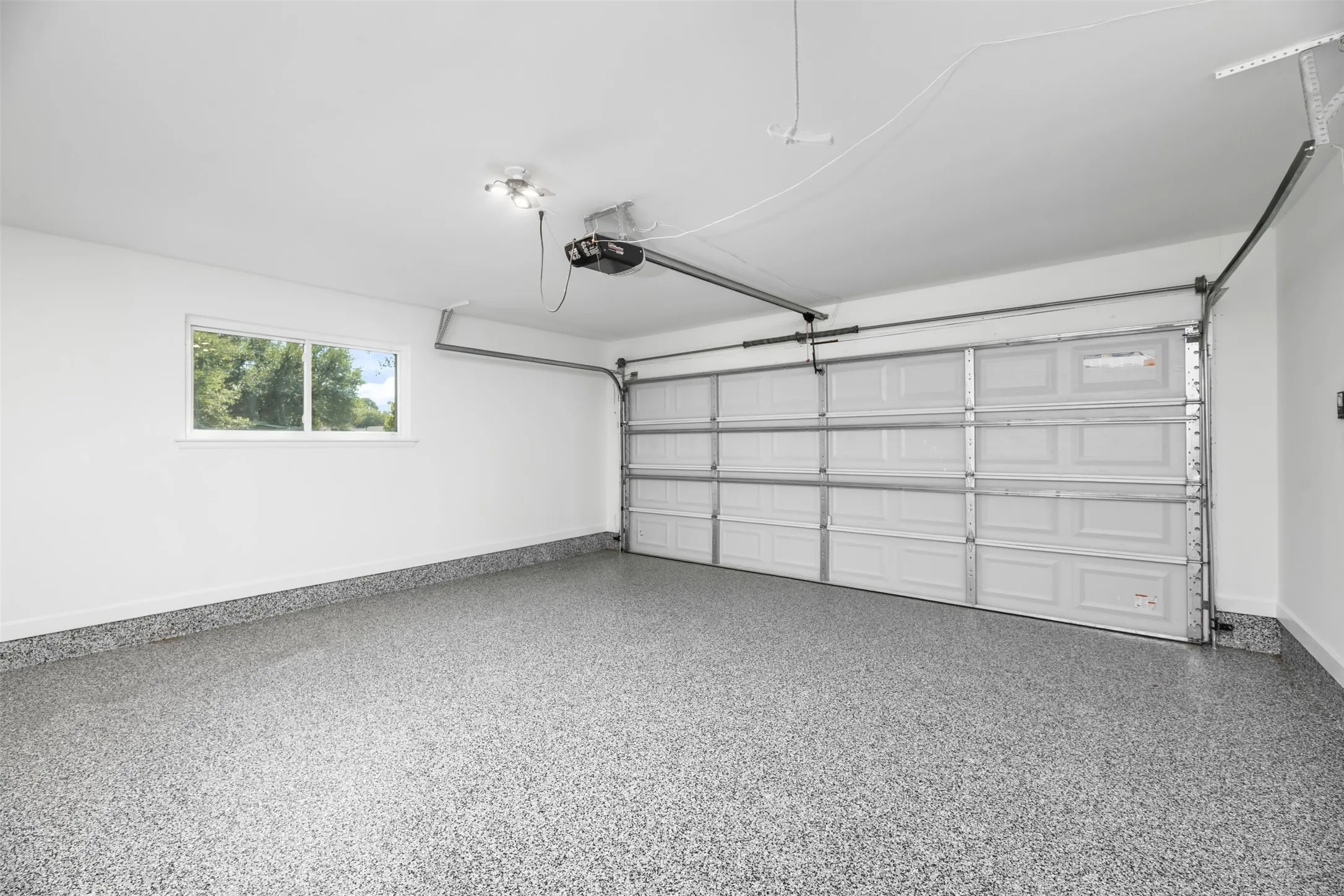 Attached two-car garage with an automatic door opener, light-colored epoxy flooring, and a window