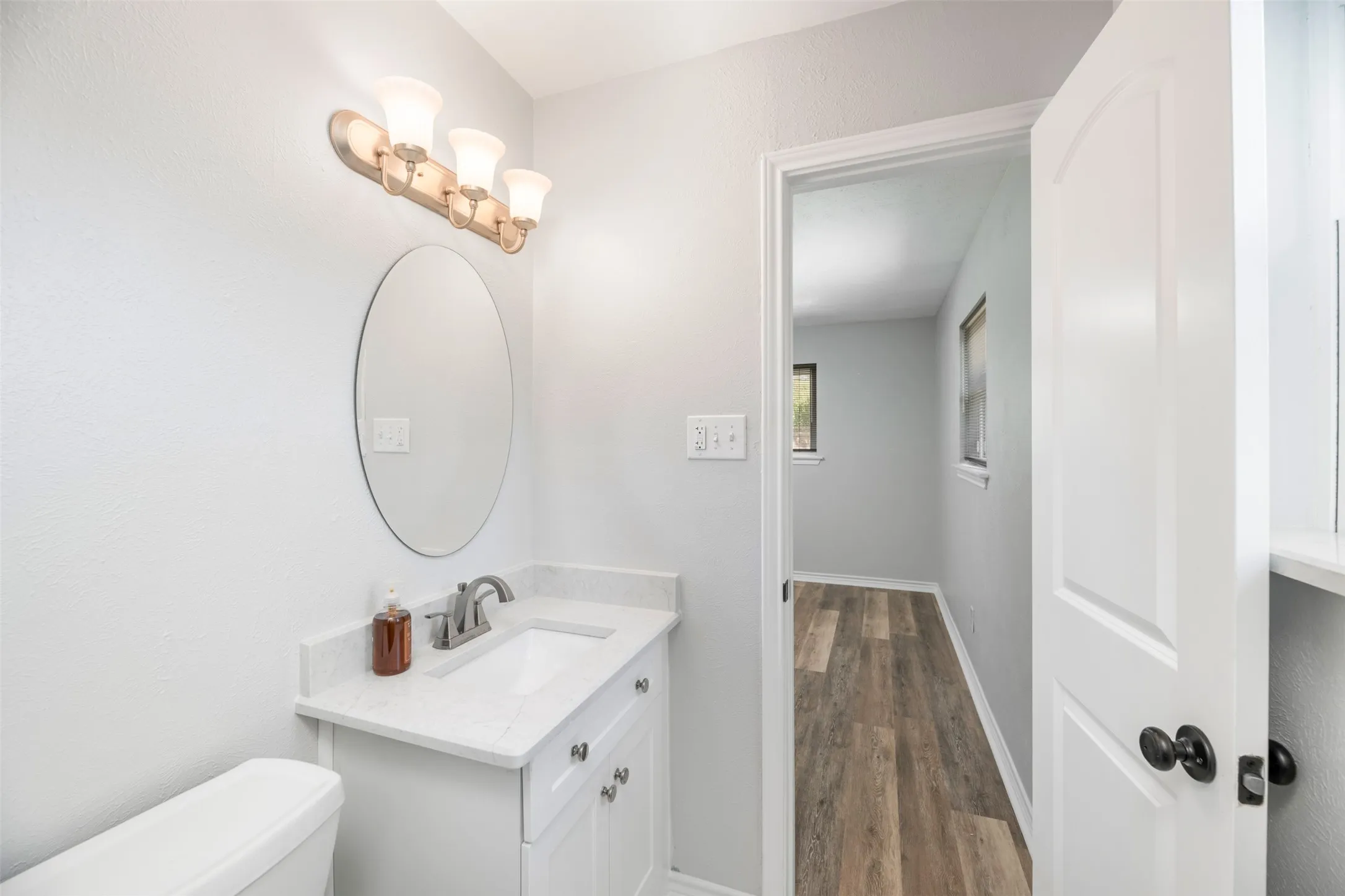 Vanity with a white countertop and integrated sink, brushed nickel faucet, and an oval mirror