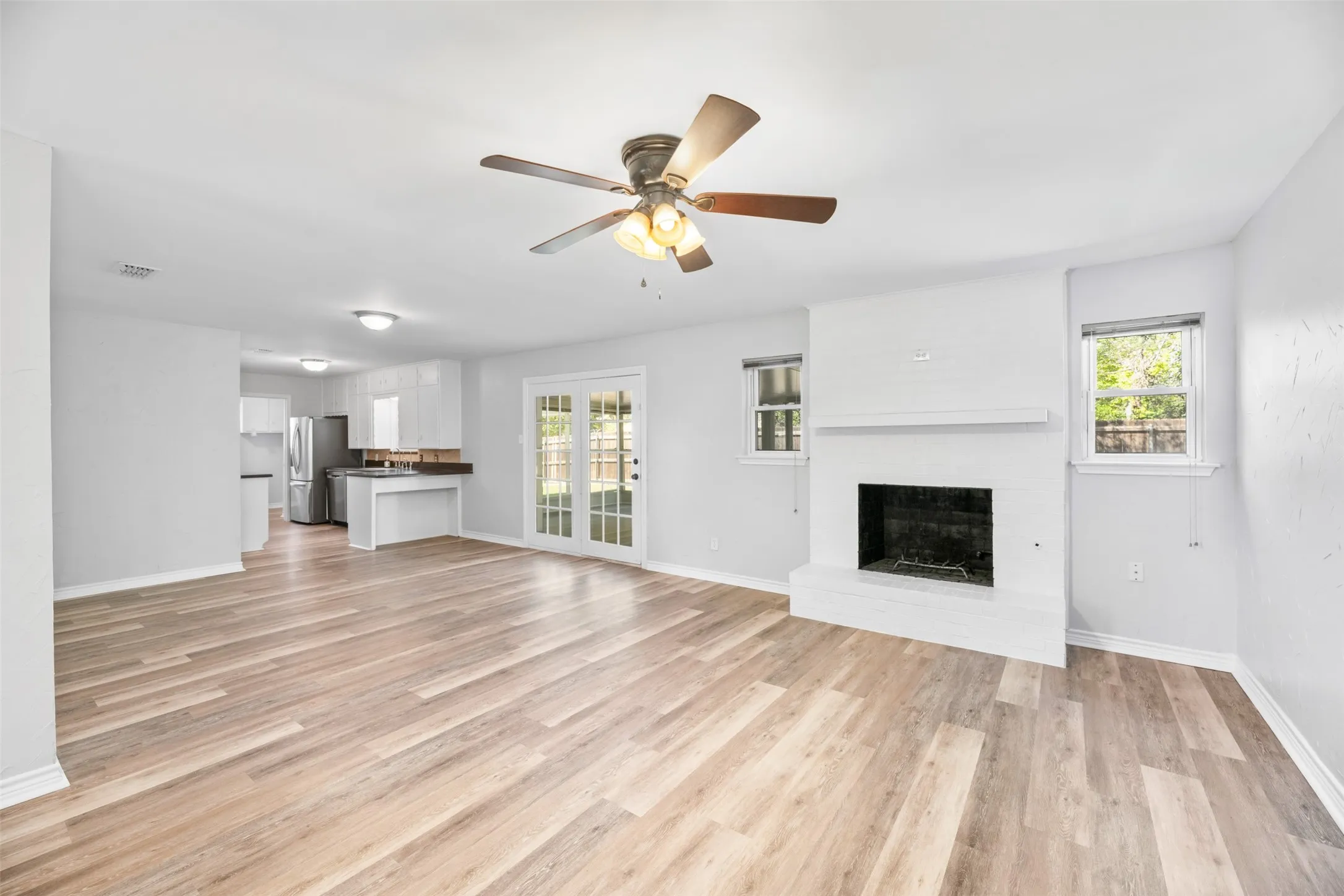 Spacious living area featuring wood-finish flooring, a white brick fireplace, and dual windows