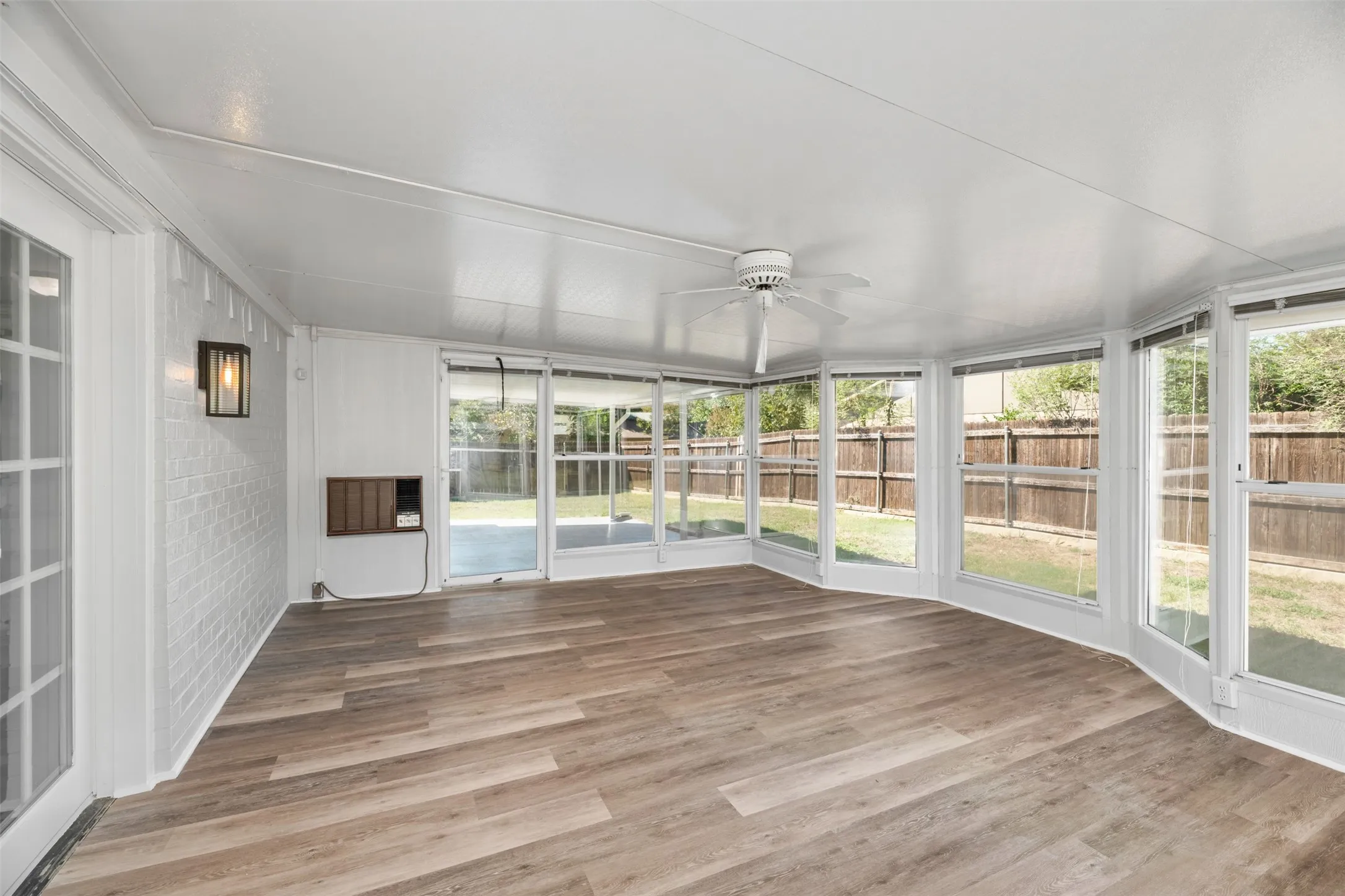 Expansive sunroom featuring wood-finish flooring, a ceiling fan, white paneled walls, and abundant natural light from multiple windows