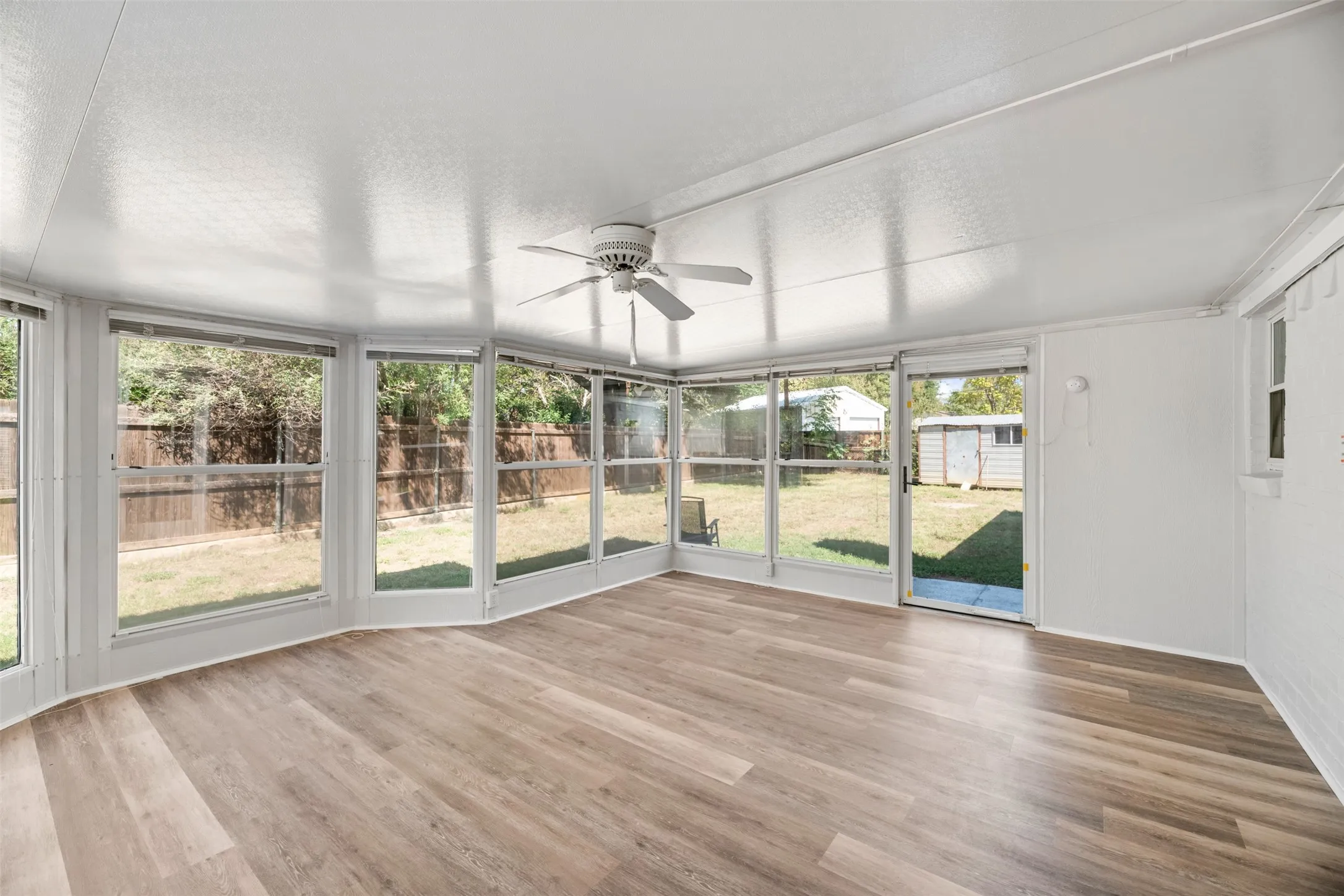 Enclosed sunroom featuring multiple large windows, wood-finish flooring, a ceiling fan, and direct access to the backyard