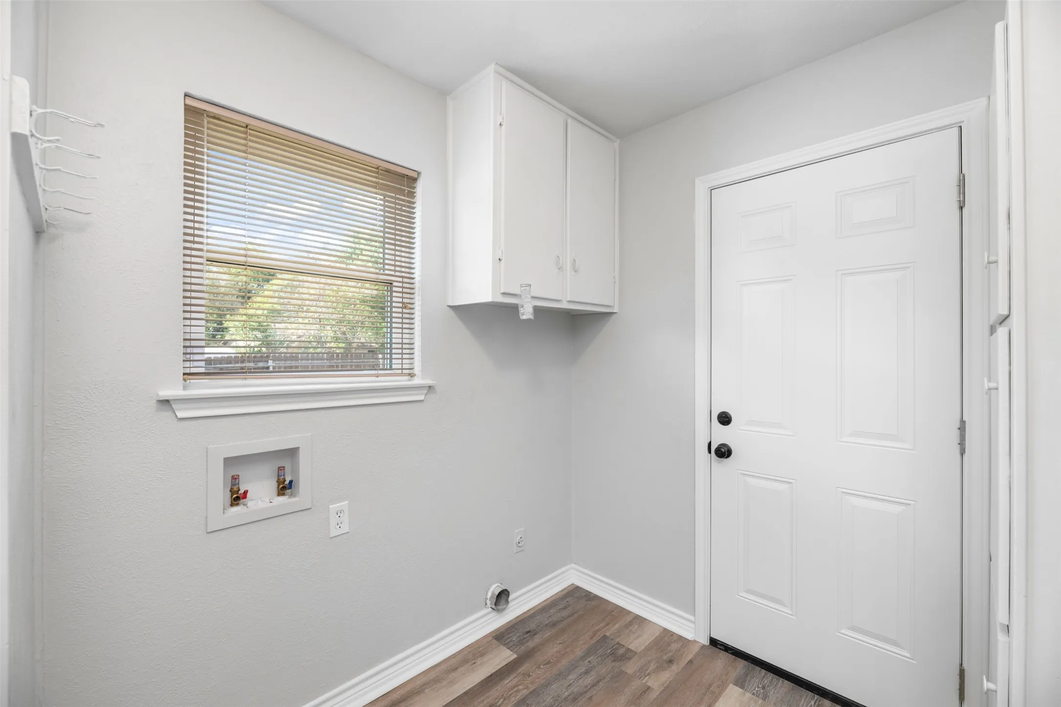 Utility room with wood-finish flooring, white paneled door, and built-in white cabinetry