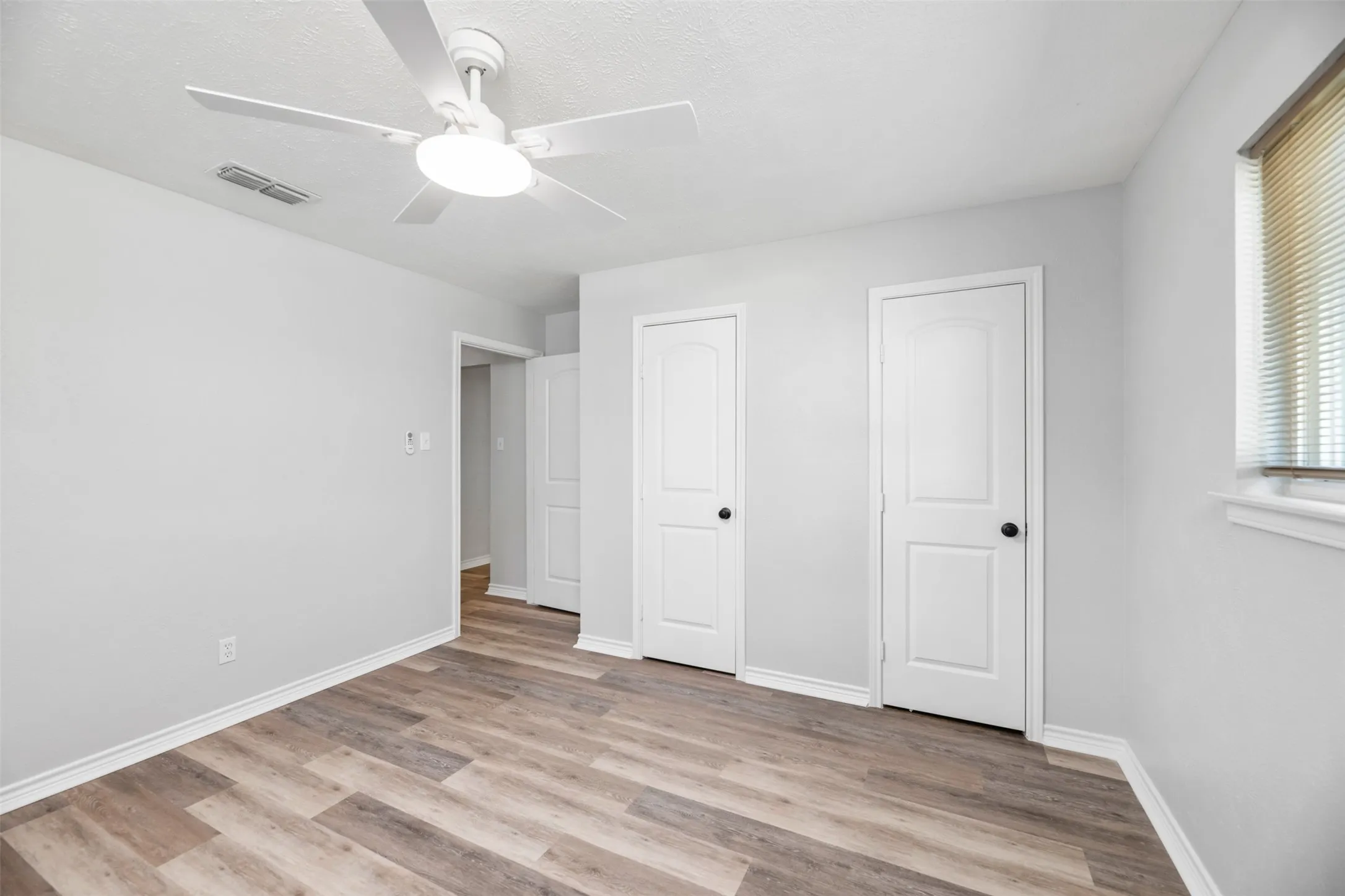 Wood-finish flooring, white walls, and a ceiling fan with integrated lighting